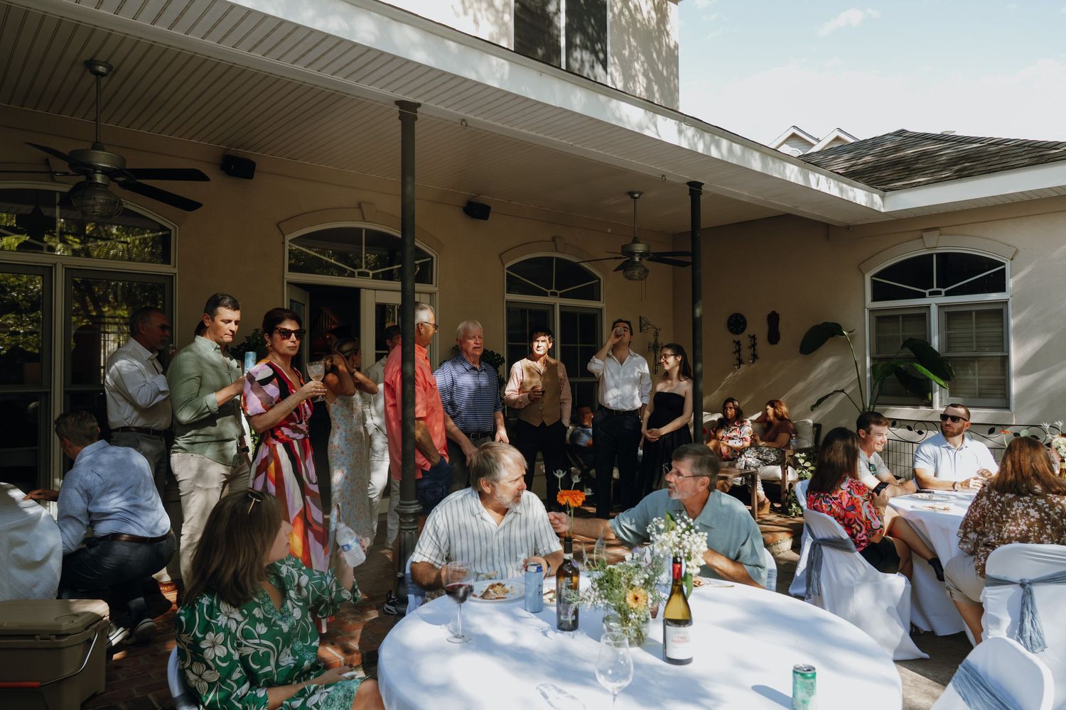 Guests mingling at an elegant outdoor daytime party on a home patio with white tablecloths.