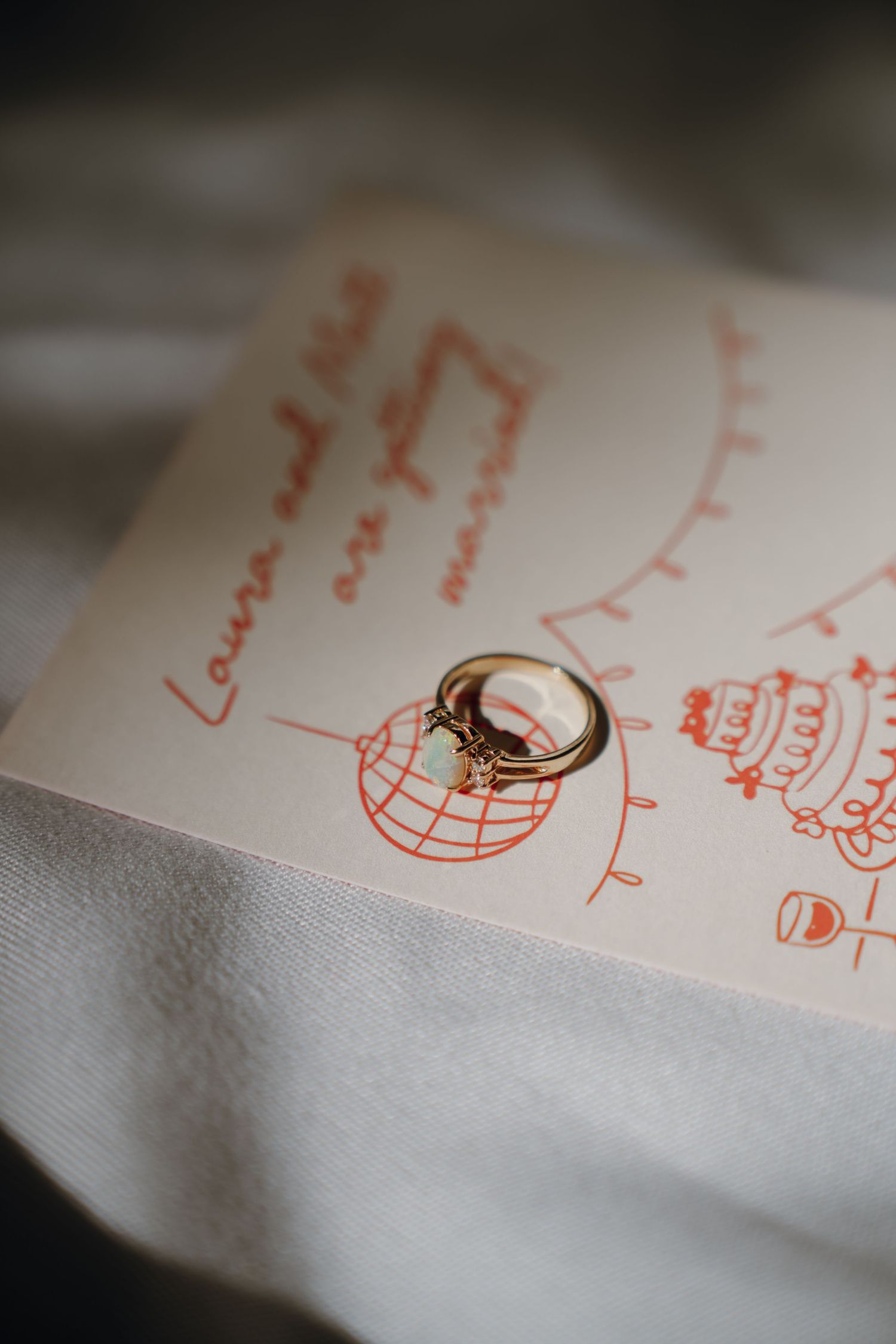 Gold engagement ring with opal stone resting on wedding invitation card reading Laura and Neil. New Orleans, Louisiana, Mississippi