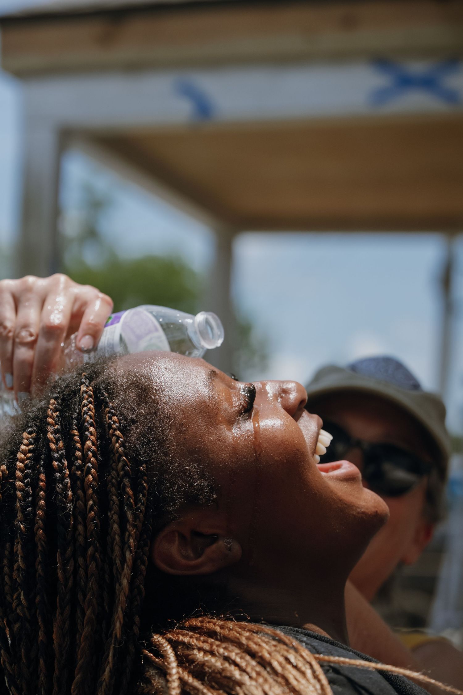 Woman laughing joyfully as water is poured over her head to cool down during outdoor volunteer work.