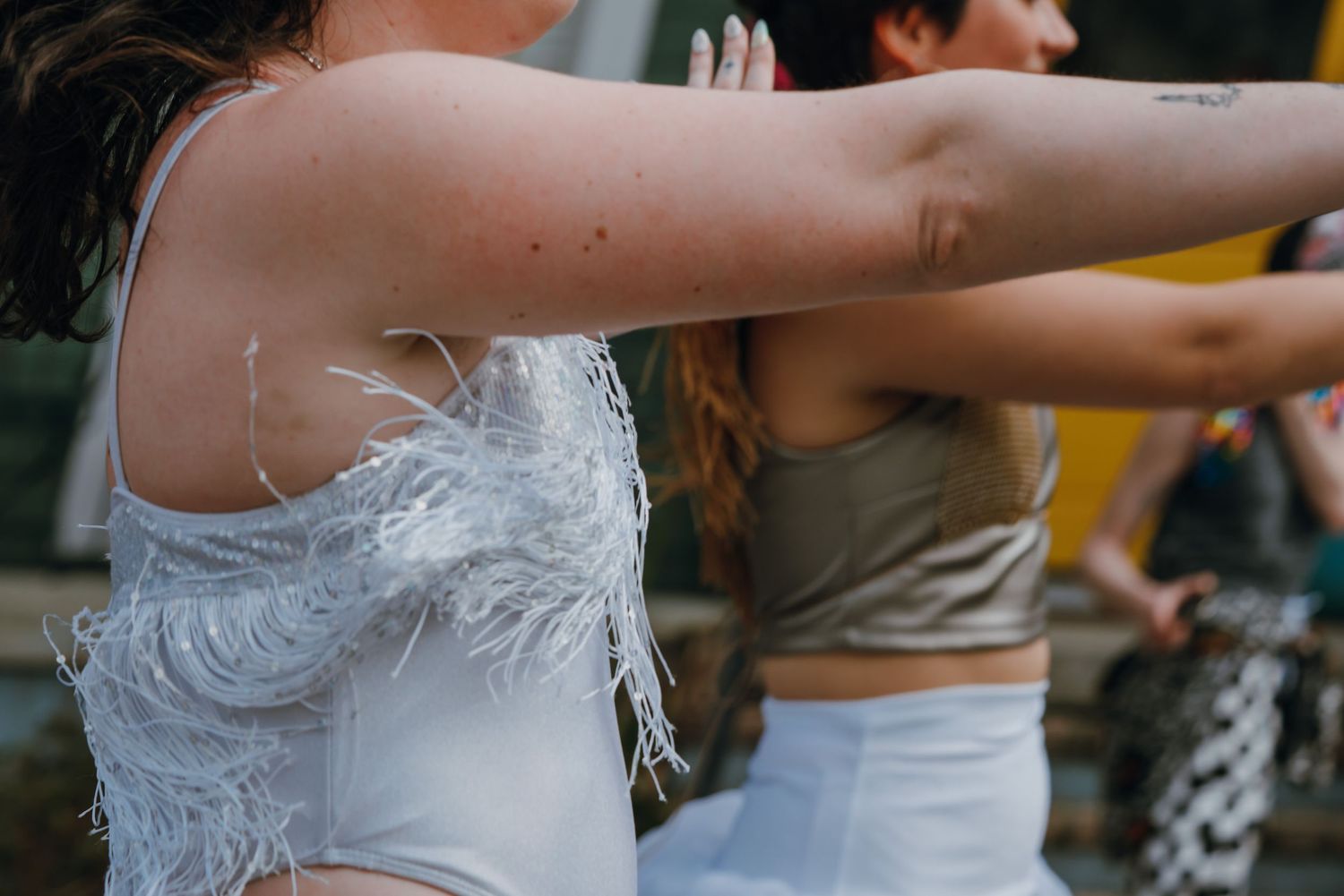 Dancer in white feathered top extends arms gracefully during an outdoor dance performance.