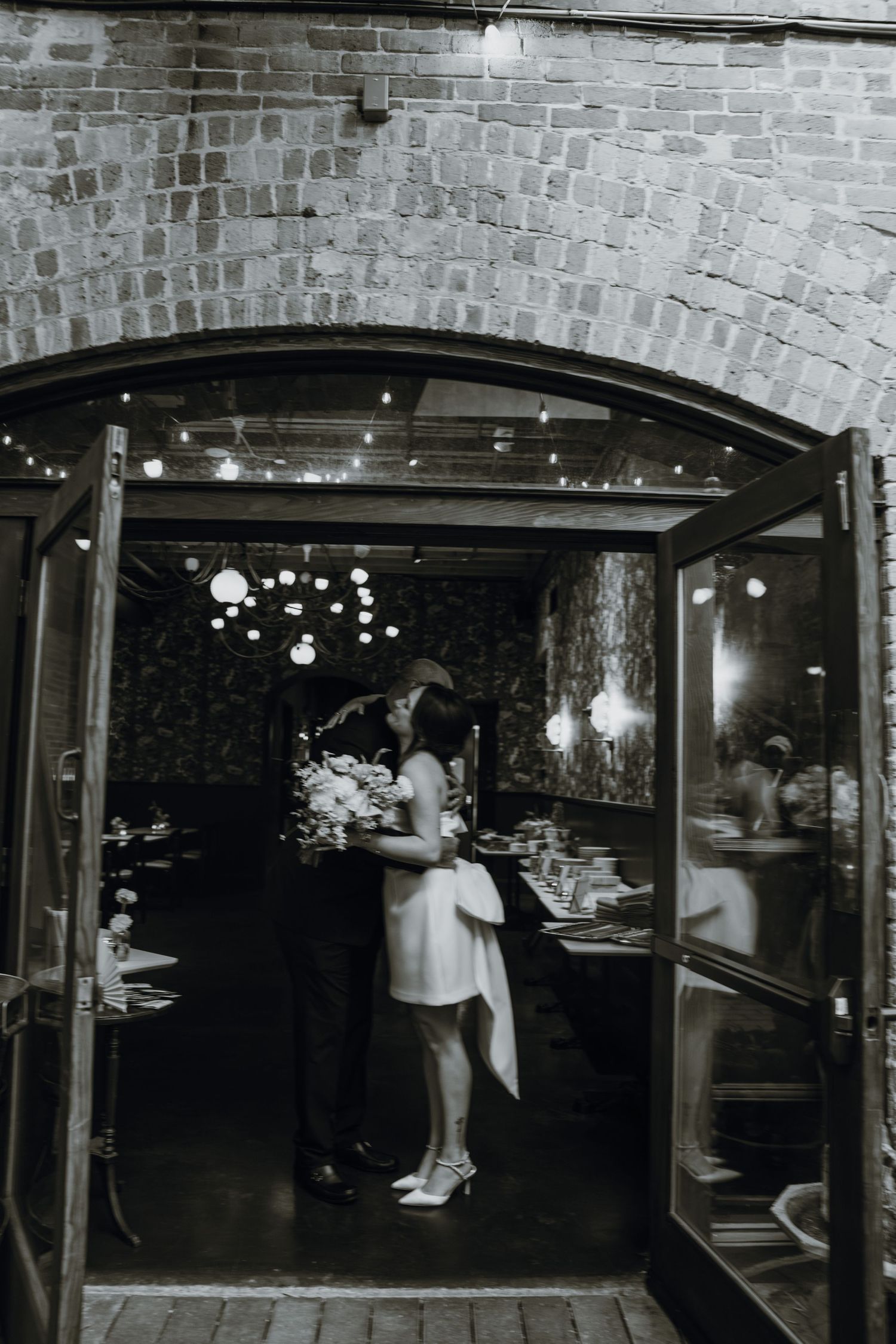 Black and white photo of bride and groom kissing in doorway of elegant brick arch wedding venue. New Orleans, Louisiana, Mississippi