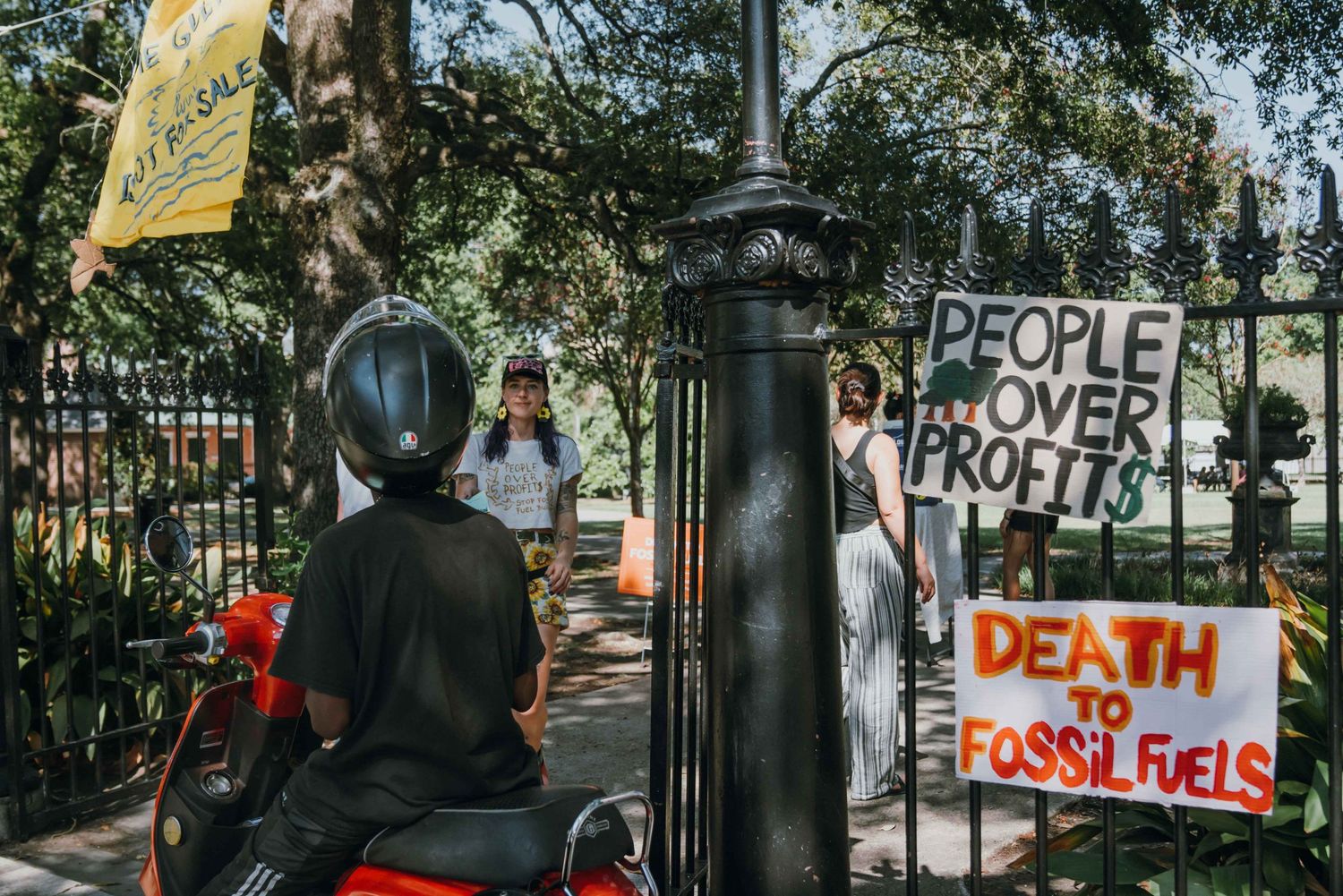 People Over Profits and Death to Fossil Fuels signs displayed at a park gate protest.