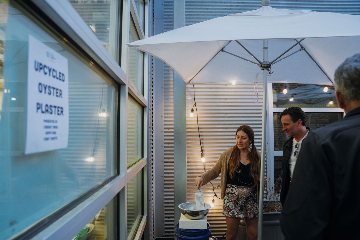 People examining upcycled oyster plaster display at an evening sustainability exhibition event.
