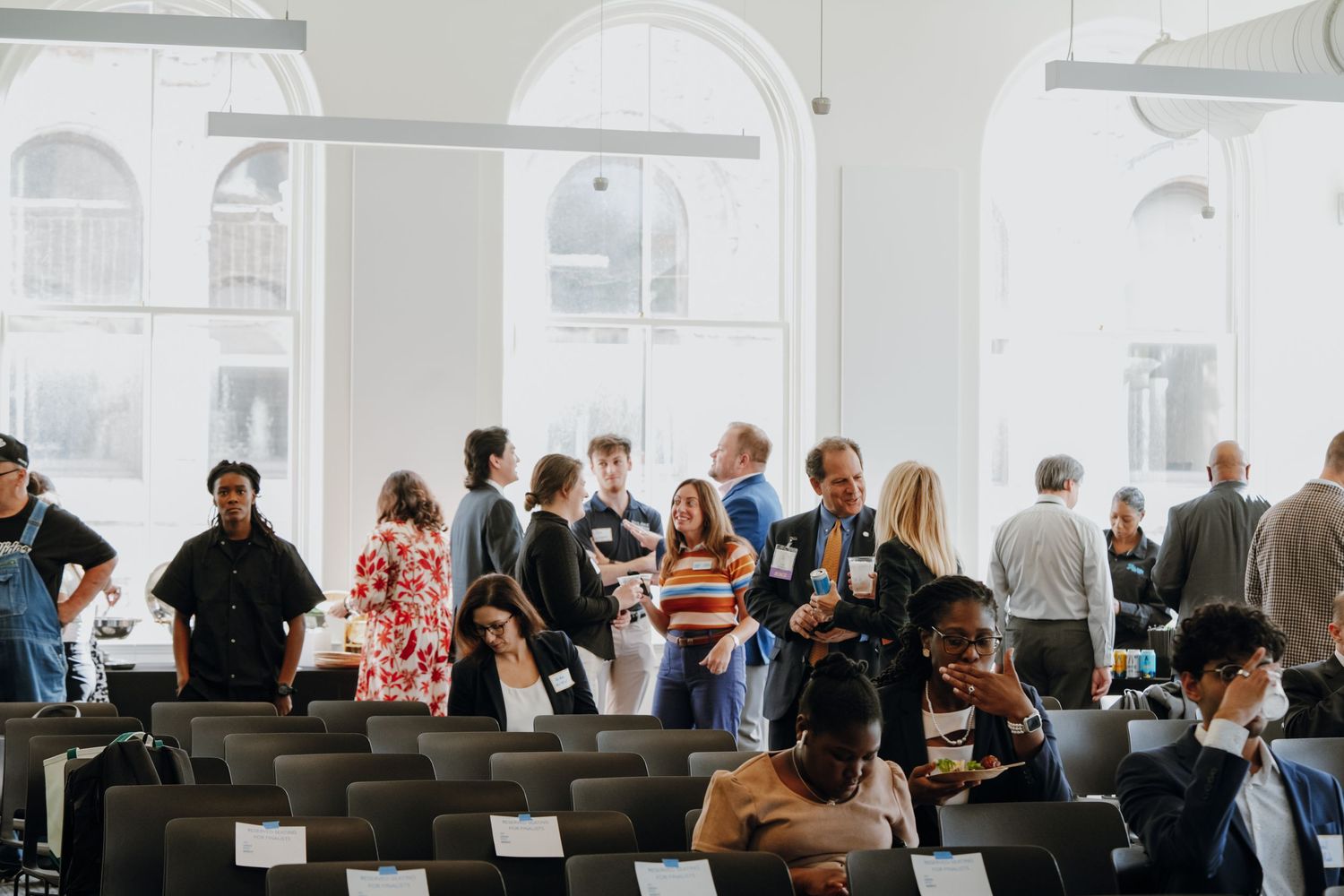 Large group of professionals networking in a bright, white-walled conference venue space.