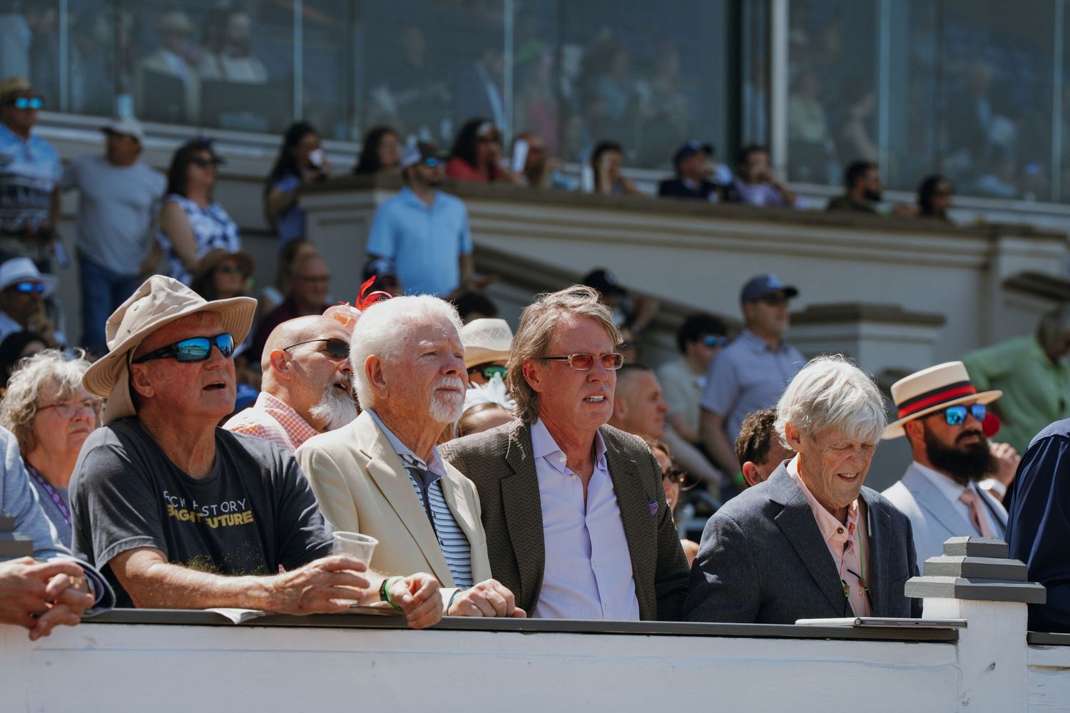 Crowd of spectators watching an outdoor sporting event on a sunny day, including older adults in casual attire.