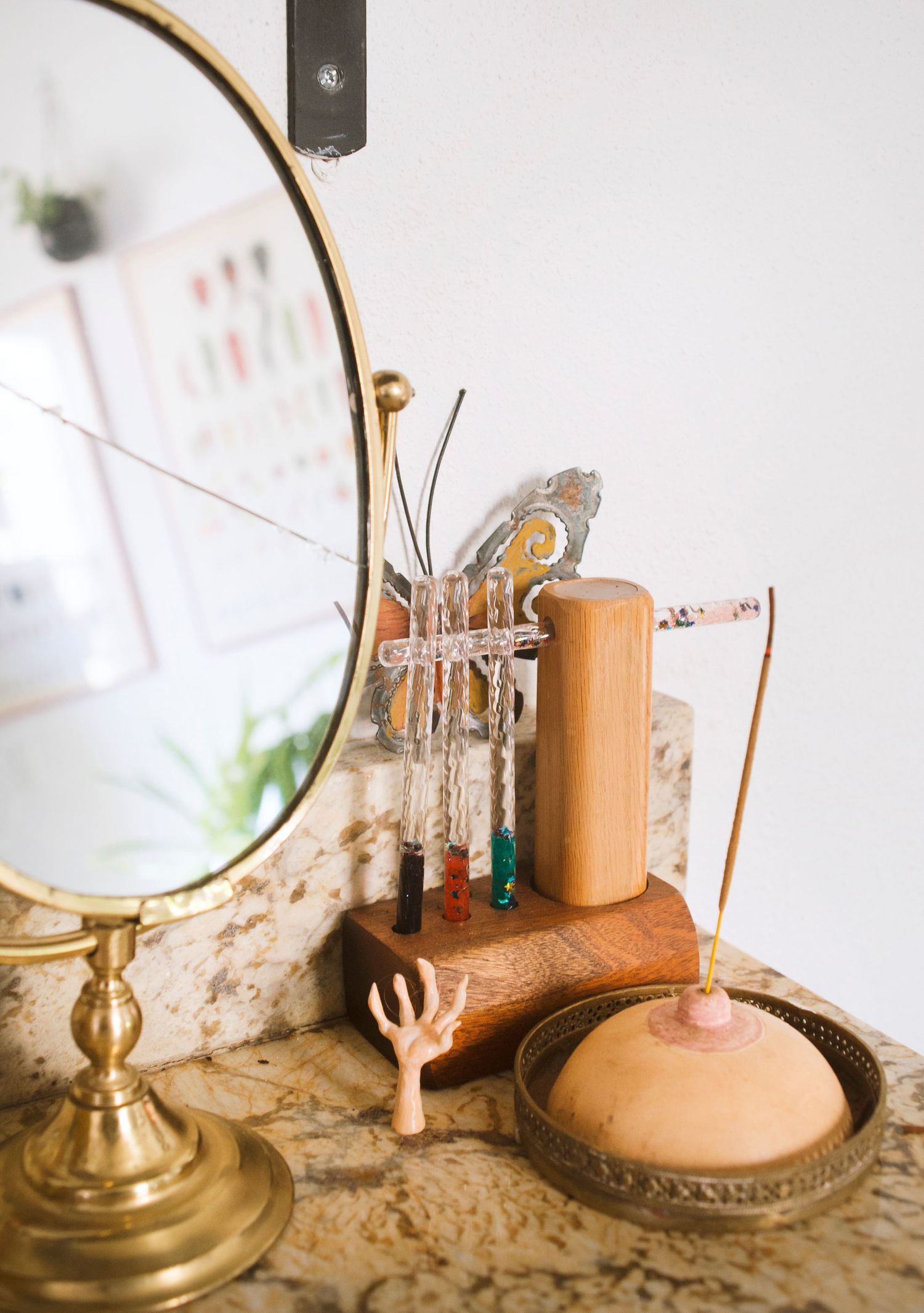 Vintage vanity display with brass mirror, wooden jewelry holder, incense, and decorative accessories on marble surface.