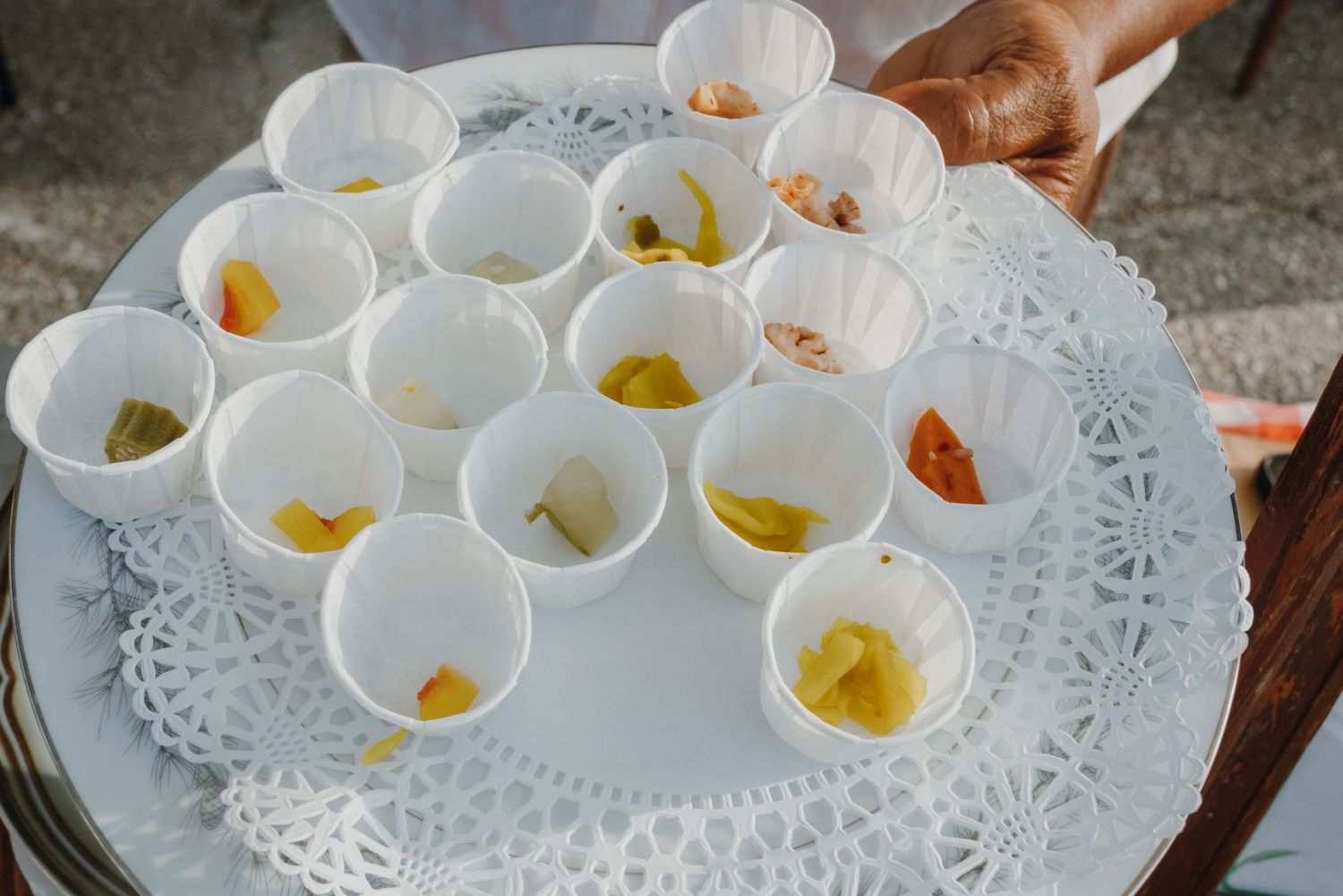 Server holding a white tray with small sample cups containing colorful food tastings at an outdoor event.