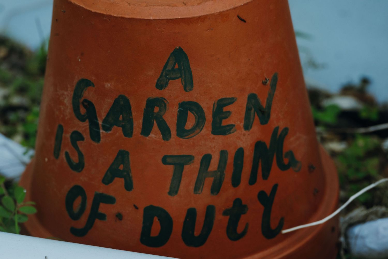 Terracotta pot with hand-painted quote reading A Garden Is A Thing Of Duty.