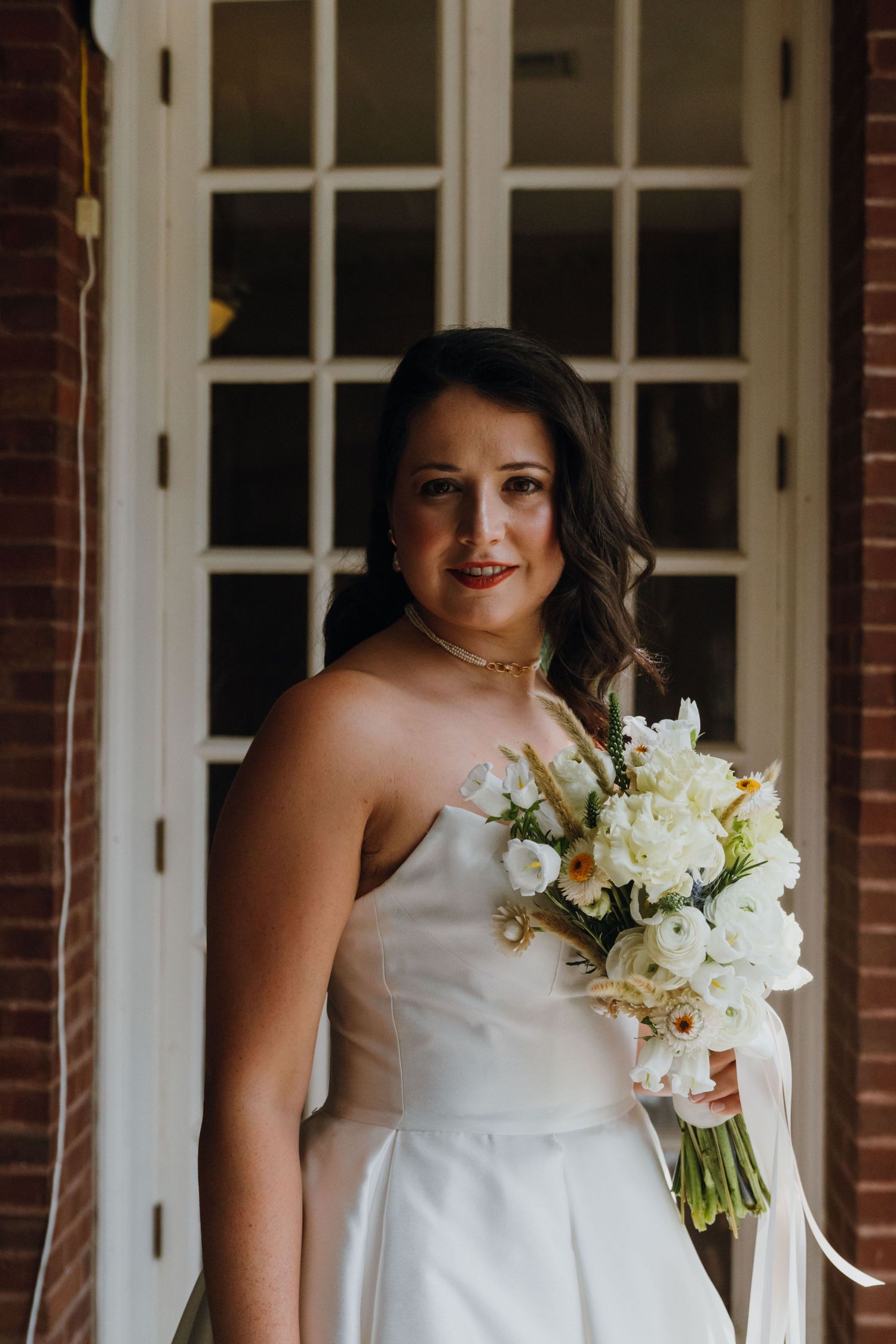 Beautiful bride in strapless white dress holding white bouquet smiling at camera outside. New Orleans, Louisiana, Mississippi