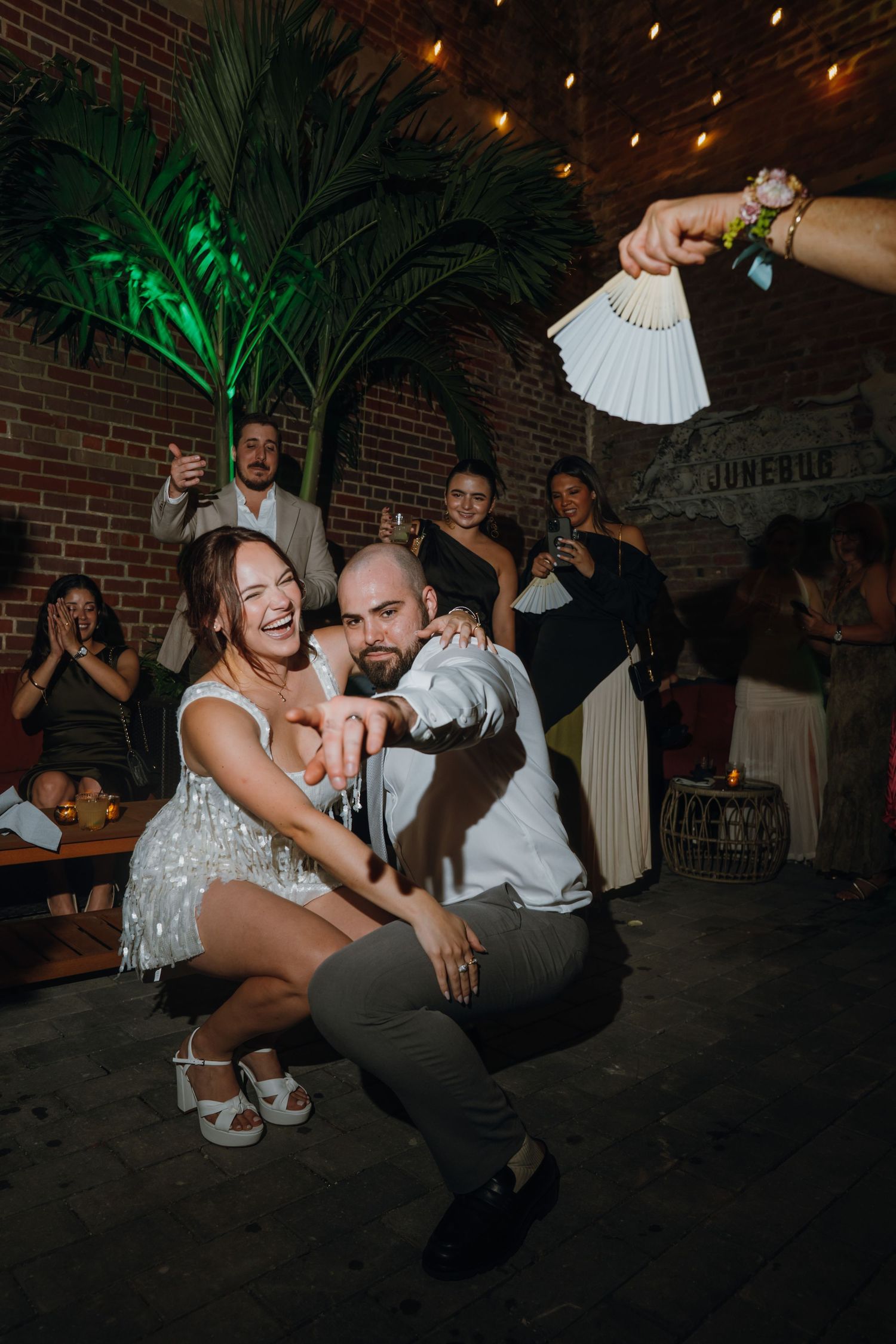 Bride and groom laugh while dancing together at lively wedding reception with string lights and guests cheering. New Orleans, Louisiana, Mis