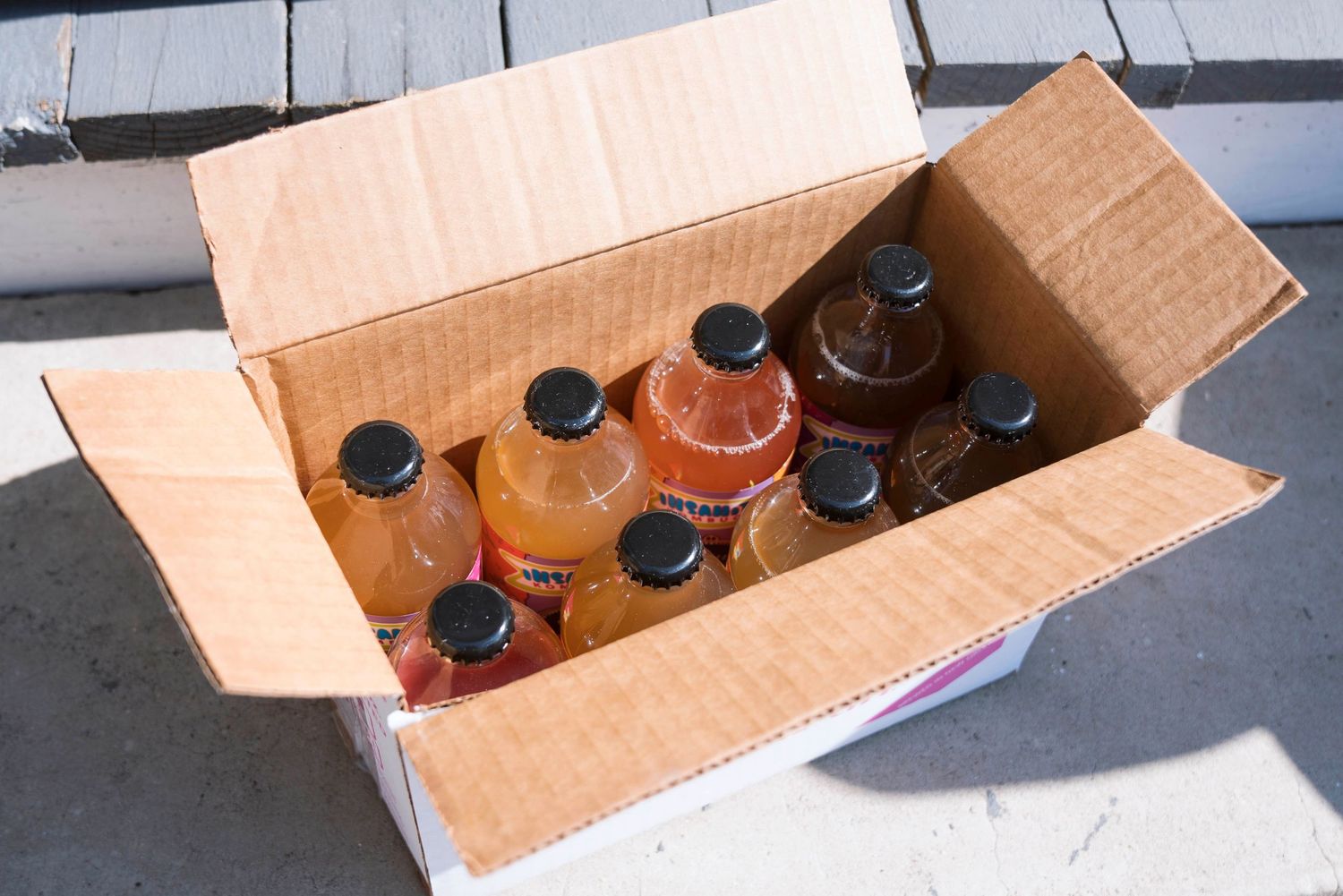Open cardboard box filled with multiple bottles of Insani-Tea Kombucha in various flavors.