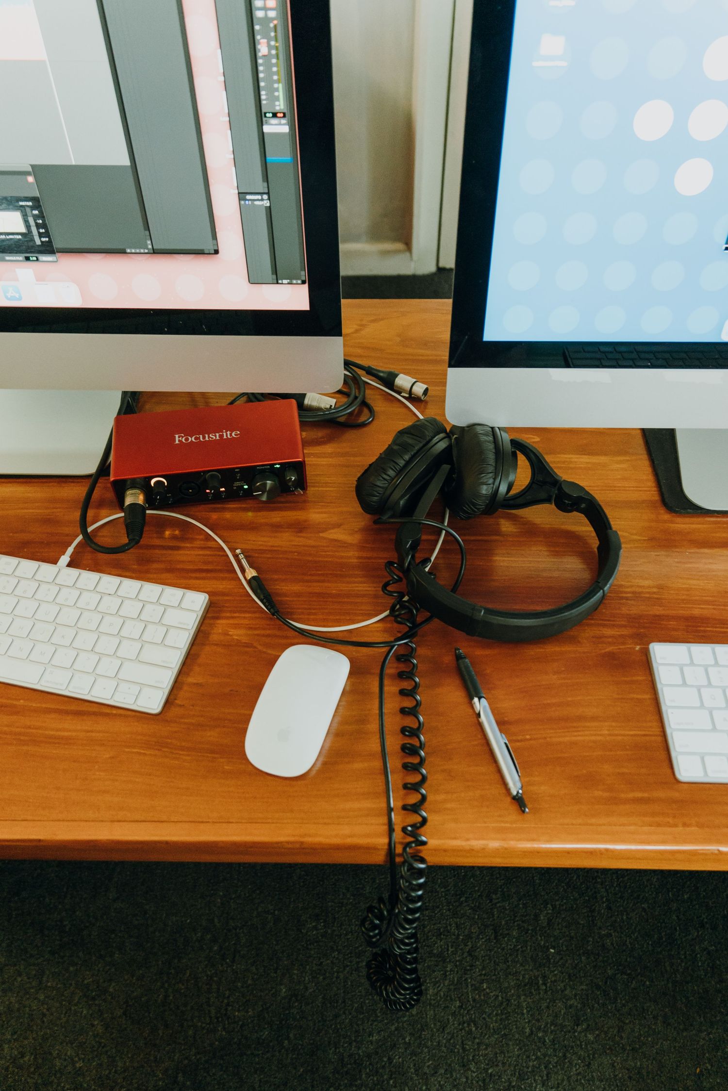 Focusrite audio interface with headphones and microphone on a wooden desk between two computer monitors.