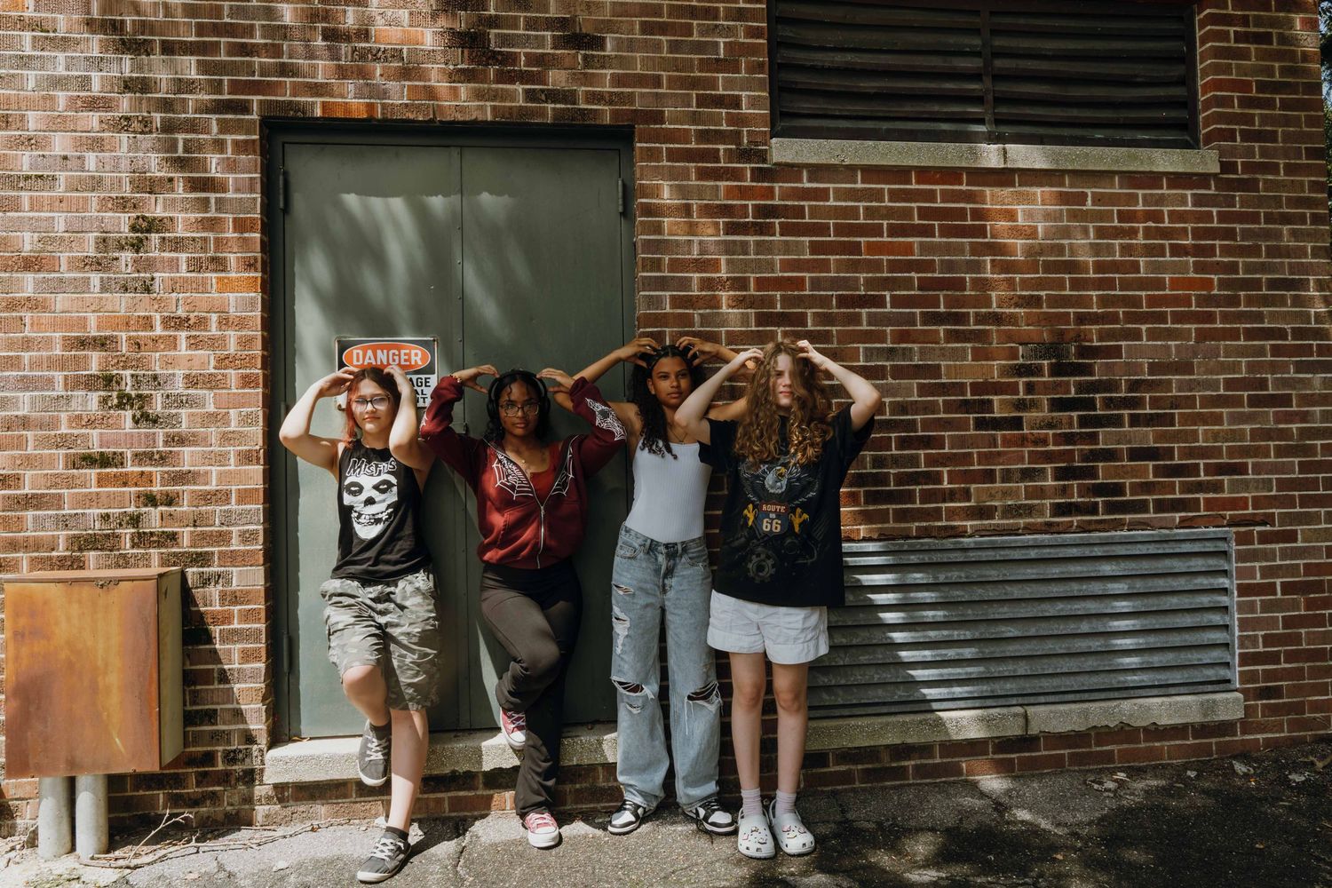 Four diverse teenage girls pose playfully against brick wall outside building in casual outfits. New Orleans, Louisiana, Mississippi