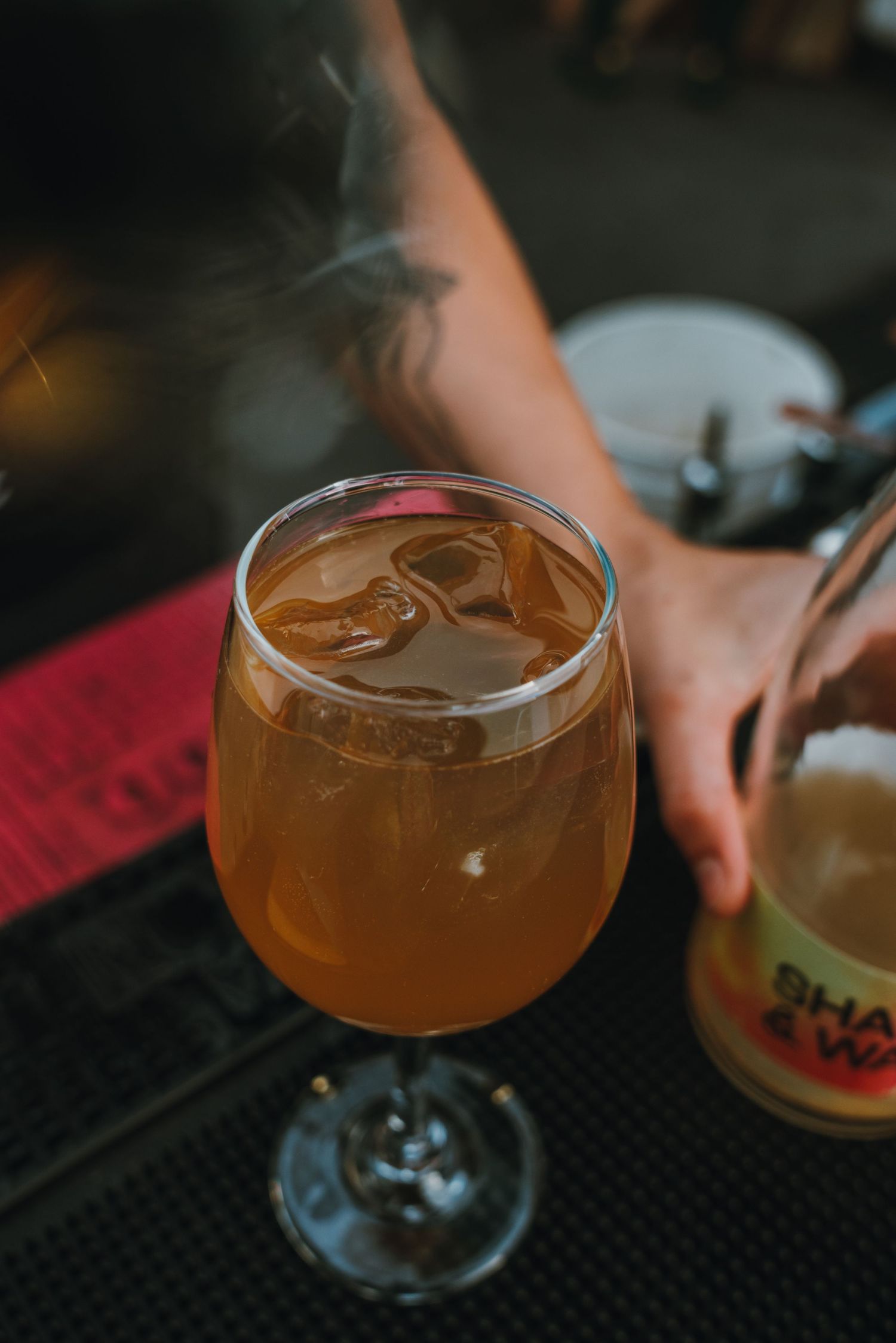 A golden amber cocktail in a wine glass with ice and steam at a bar.
