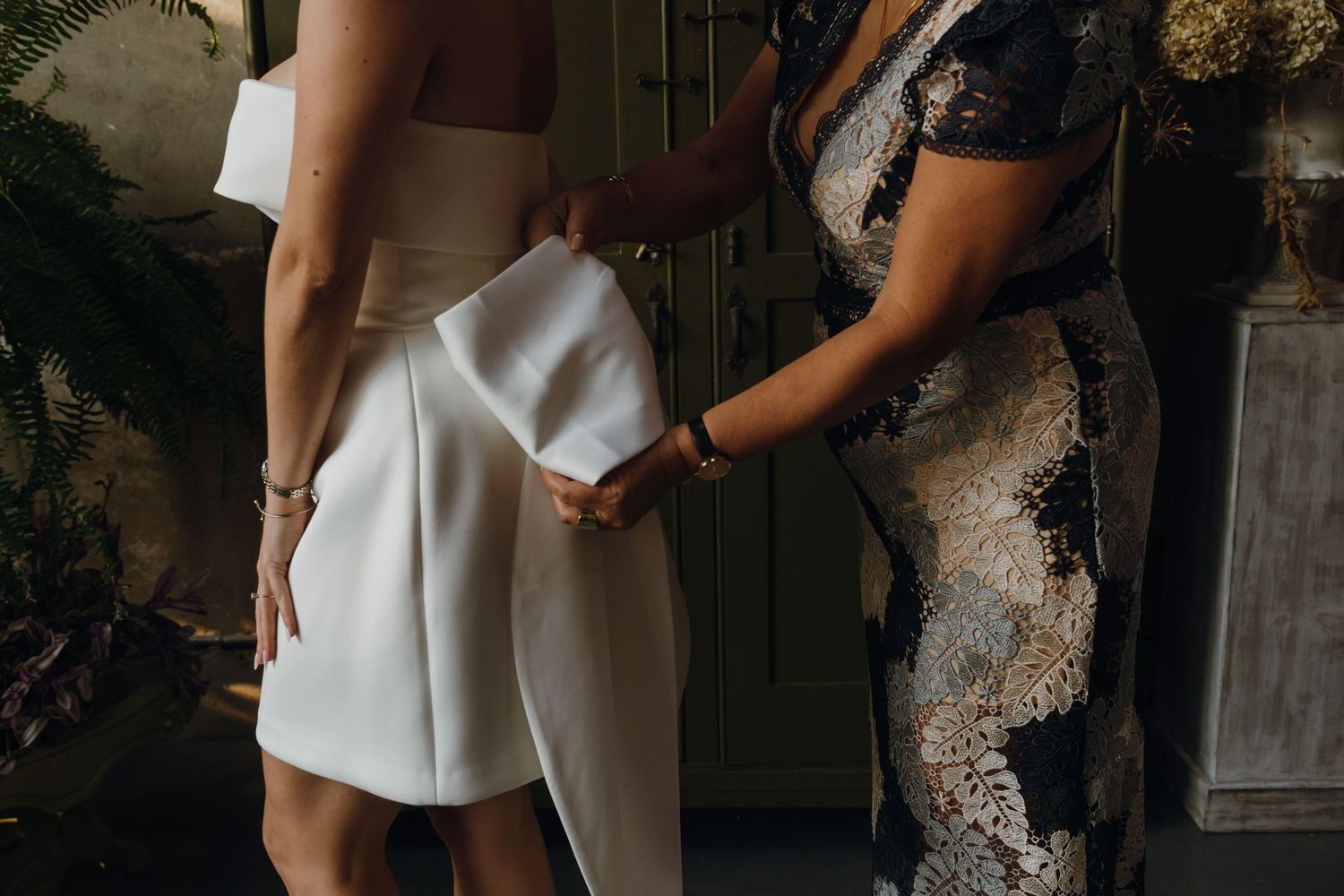 Close-up of mother helping bride adjust white strapless mini wedding dress from behind.