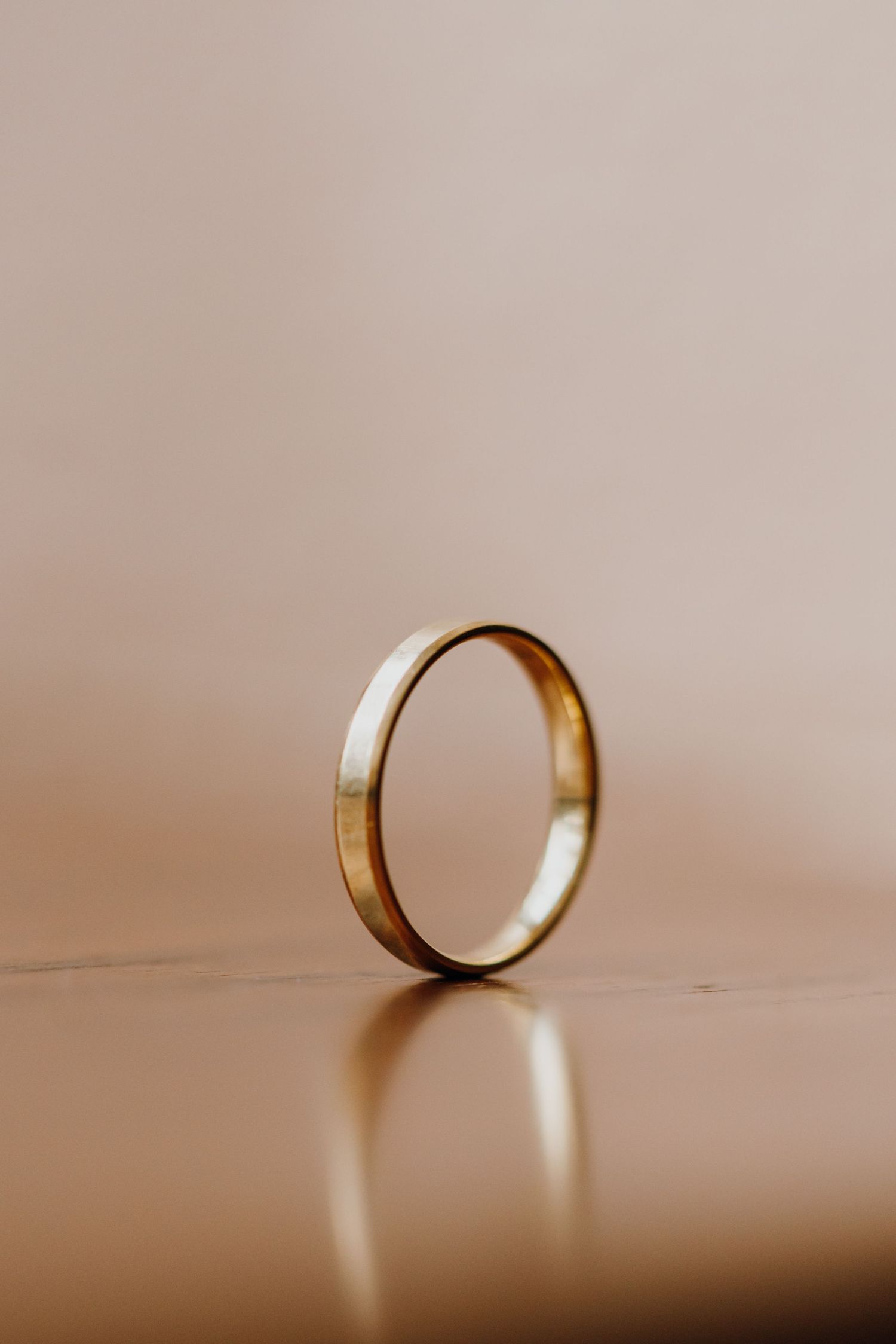 Simple gold wedding band standing upright on reflective beige surface with soft background. New Orleans, Louisiana, Mississippi