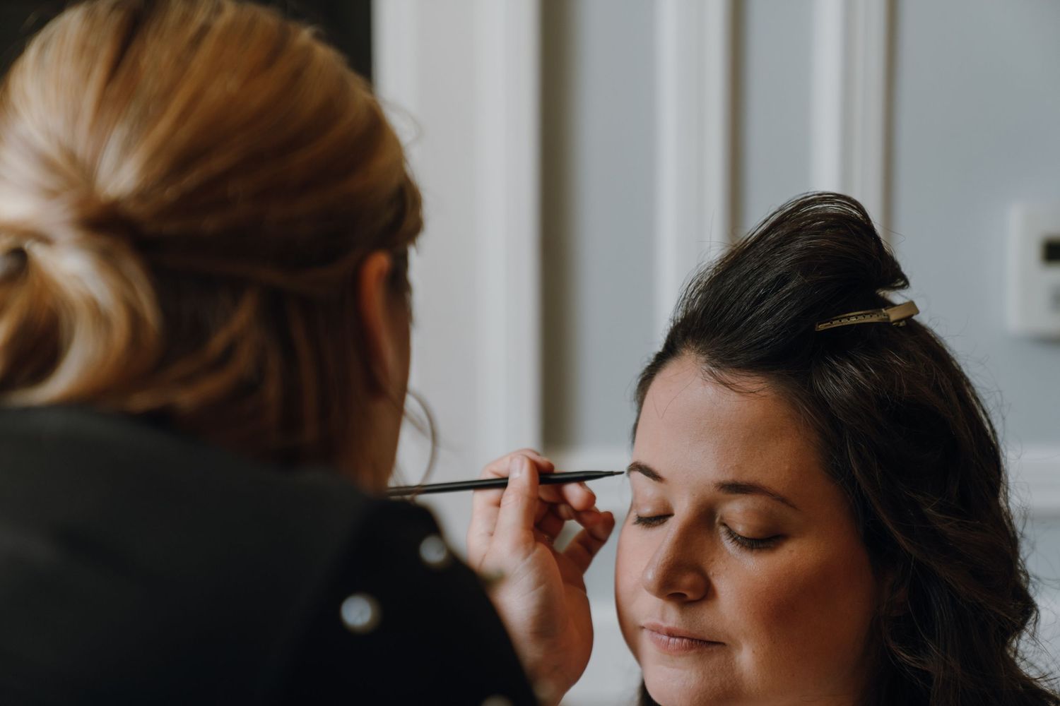 Makeup artist applying eye makeup to a dark-haired bride during wedding preparations. New Orleans, Louisiana, Mississippi