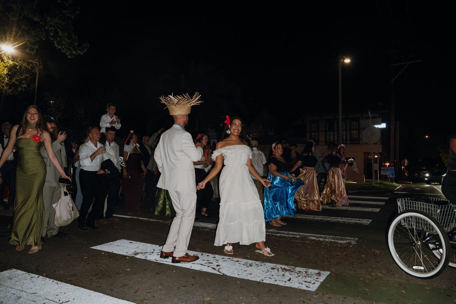 Couple in traditional attire dancing on street crosswalk at night during festive outdoor wedding celebration.