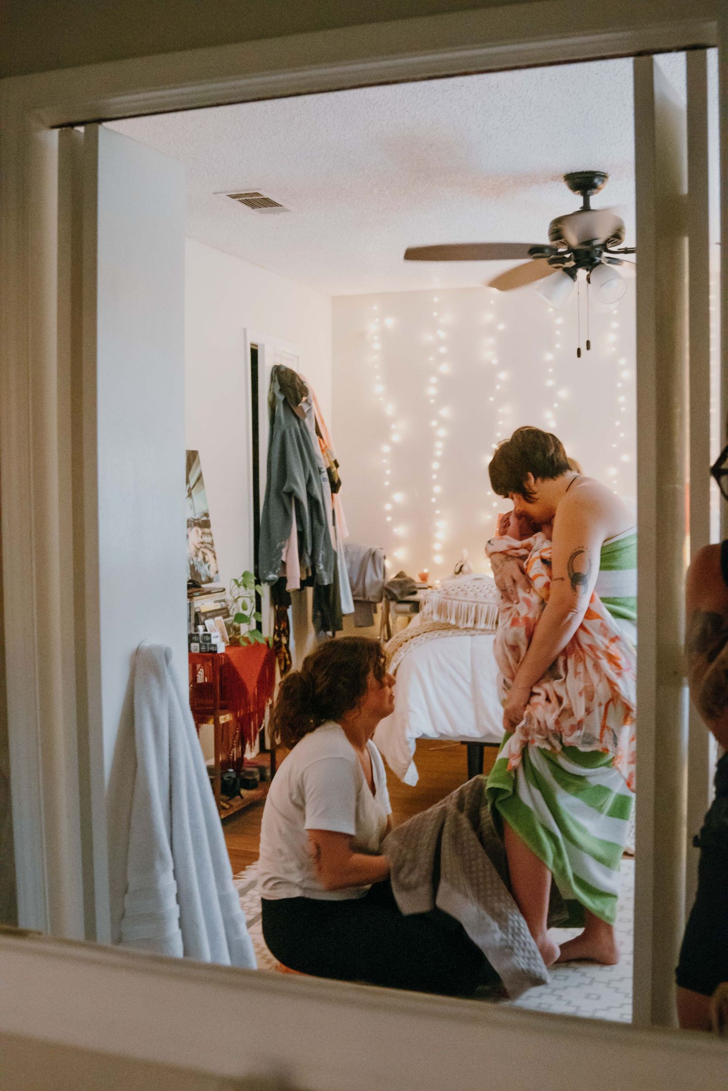 View through window of midwife assisting mother with newborn in fairy light bedroom. New Orleans, Louisiana, Mississippi