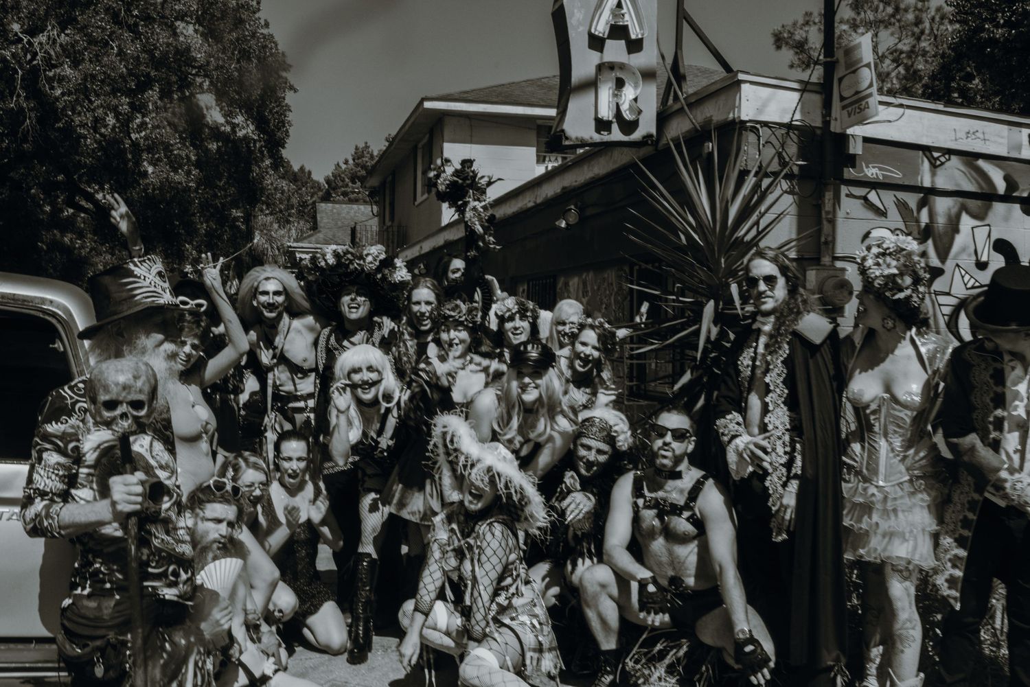 Black and white photo of a wedding party matrimony homies  group photo in elaborate wedding costume attire at an outdoor dive bar wedding