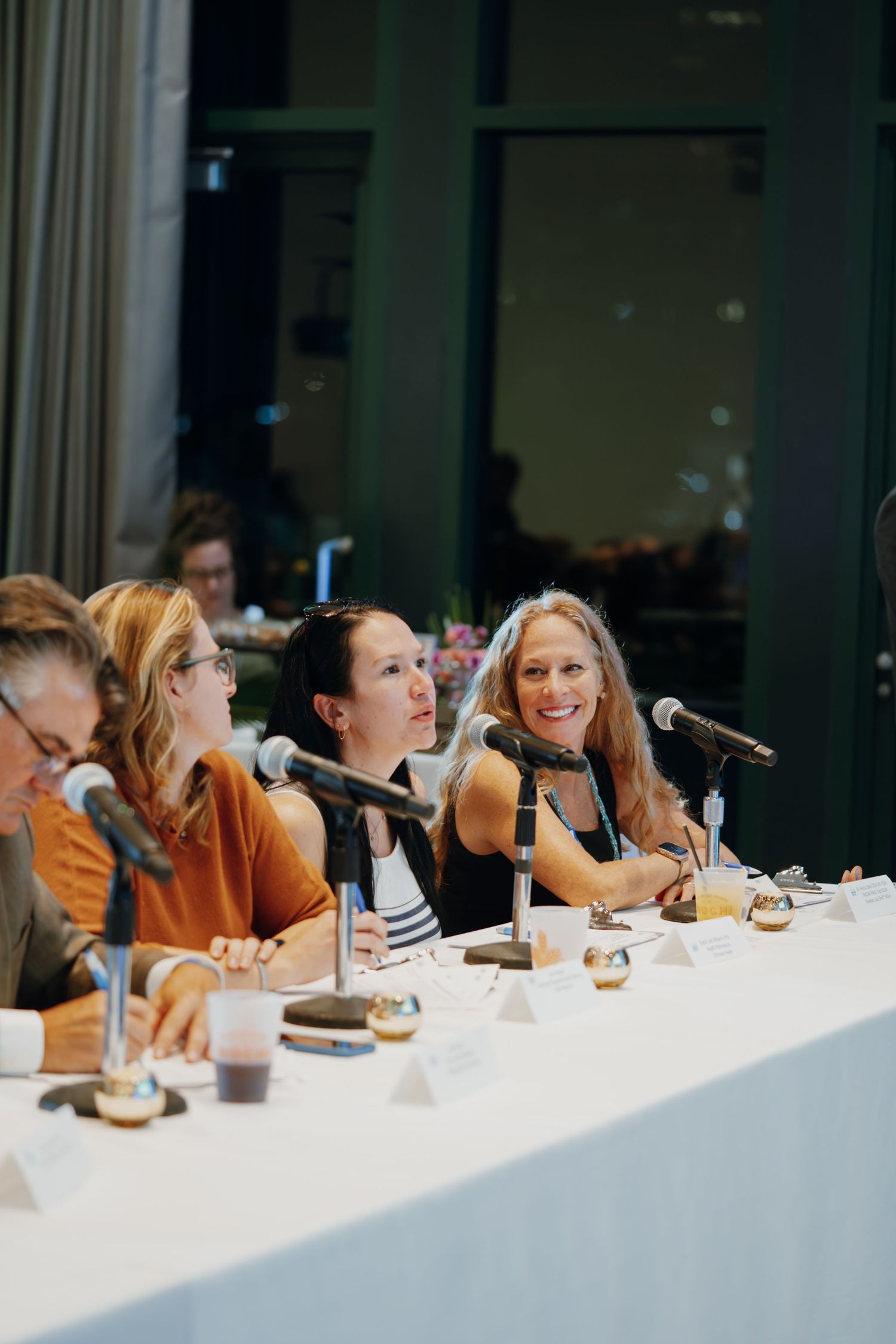 Panel of four women speak at conference table with microphones during a professional forum.