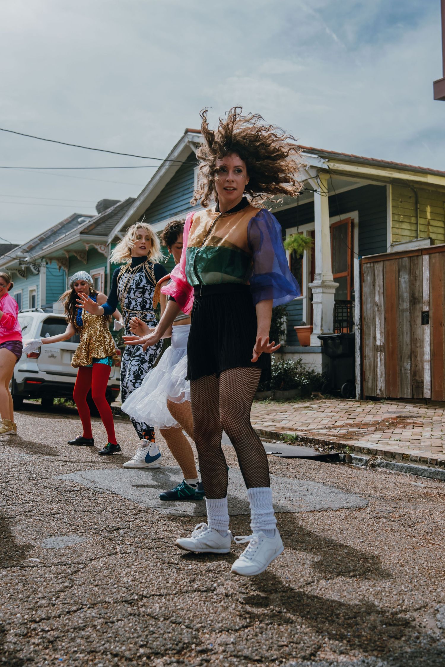 Energetic woman dancing in the street with flowing hair and colorful outfit.