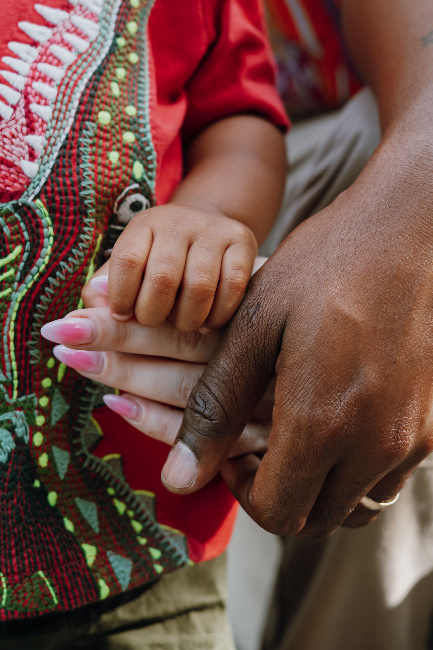Close-up of a toddler holding parents hands, showing pink manicured nails and a gold wedding band.
