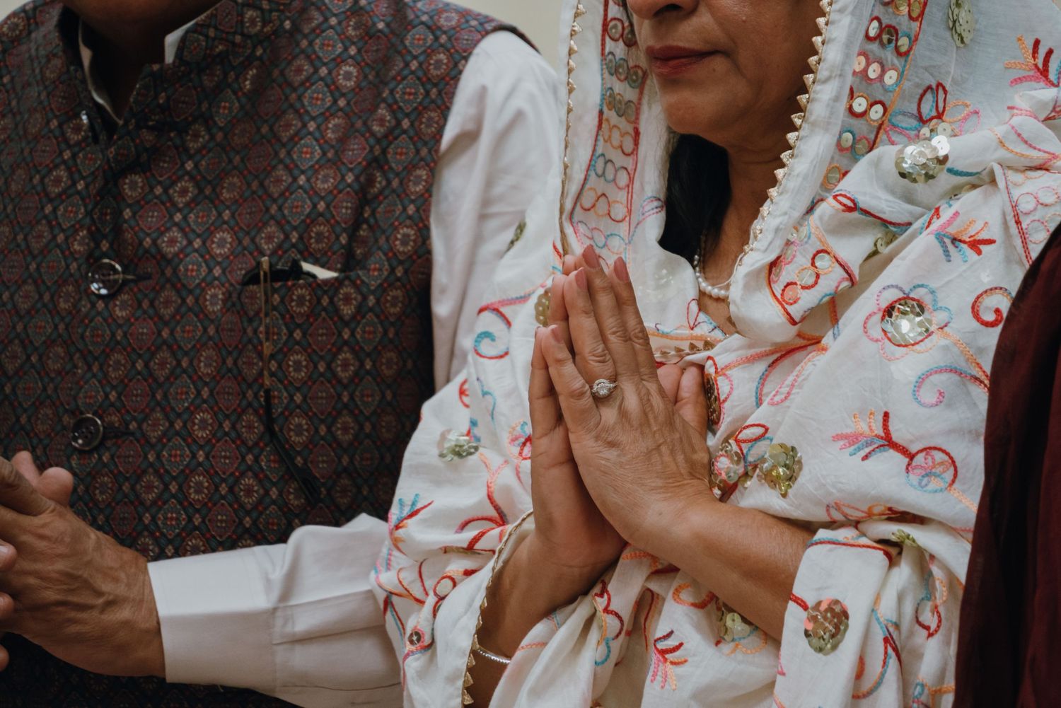 Woman in embroidered white salwar kameez holds hands in Namaste prayer gesture at a Sikh wedding.