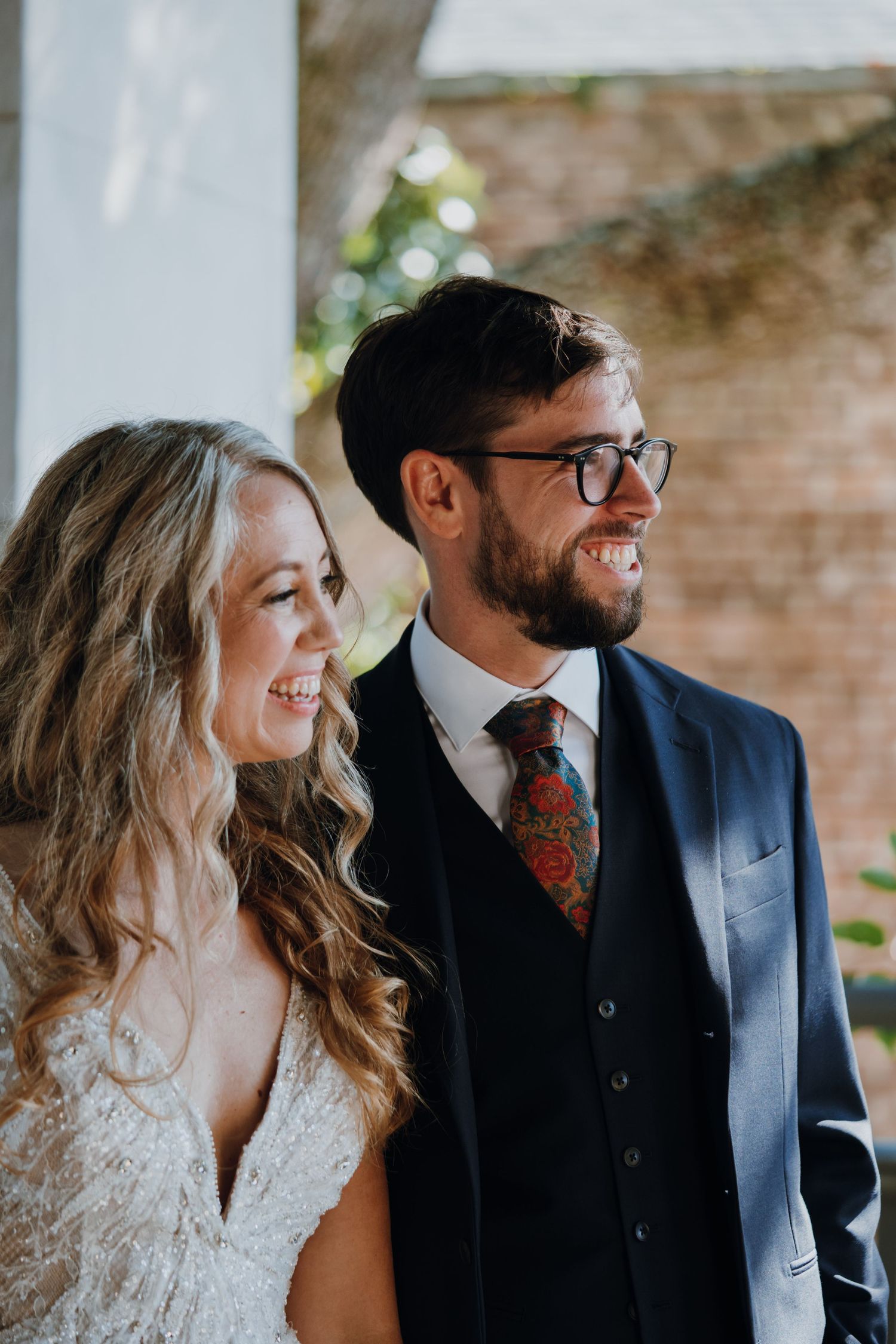 Smiling bride and groom in navy suit with floral tie sharing joyful wedding moment.