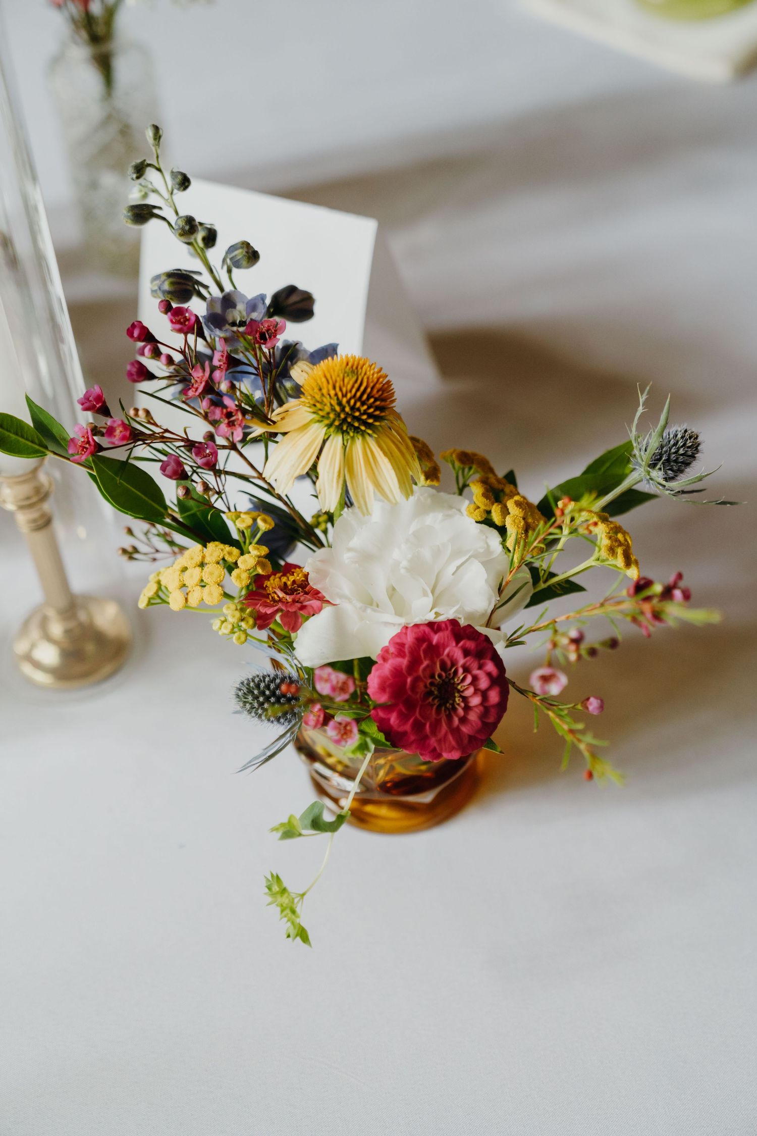 Colorful wildflower wedding centerpiece with dahlias, echinacea, and thistles in a gold vase on white linen. New Orleans, Louisiana, Mississ