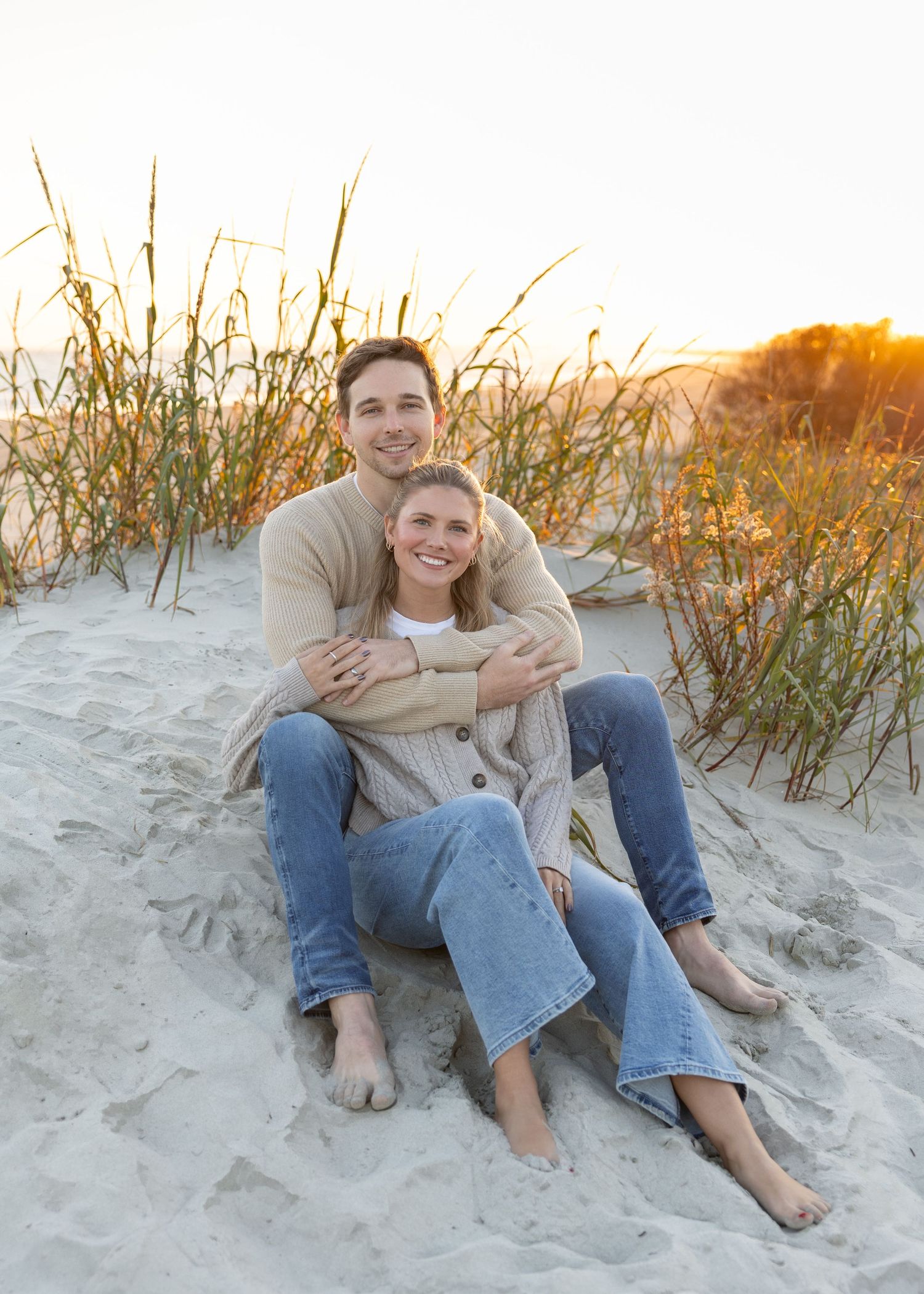 A couple sits together on beach sand dunes during golden hour.