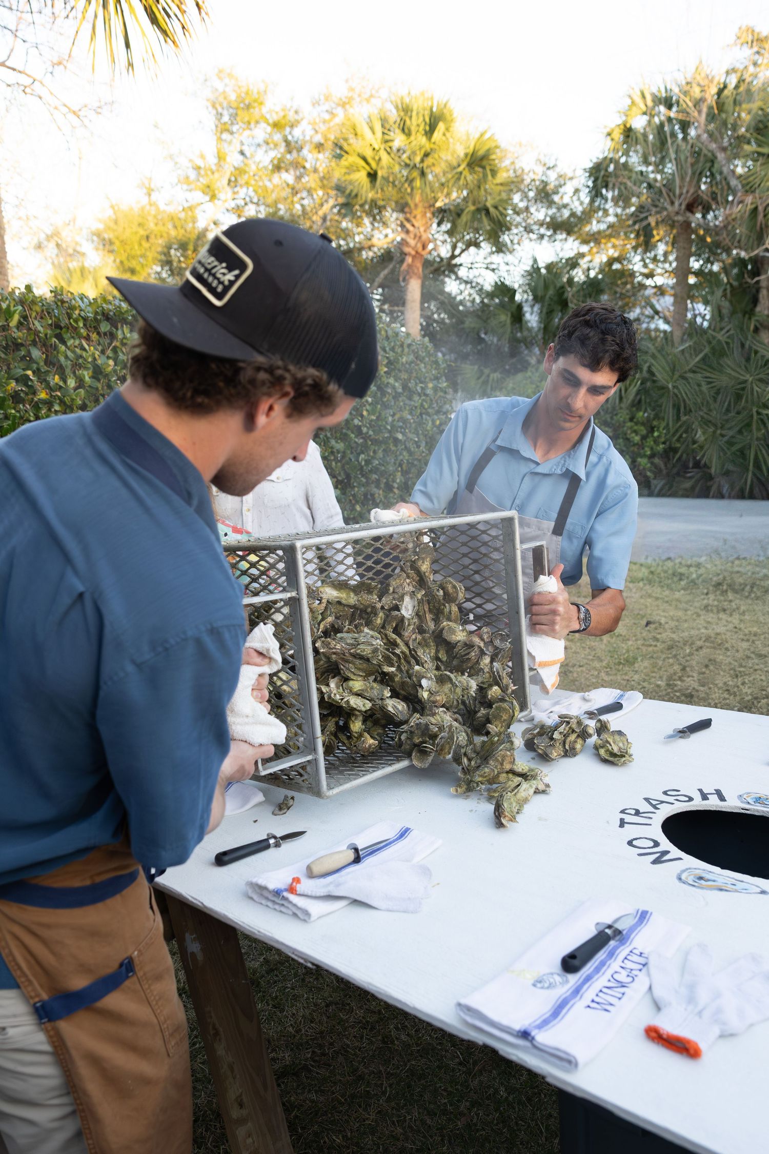 People gathered around table examining and working with oysters during outdoor event.