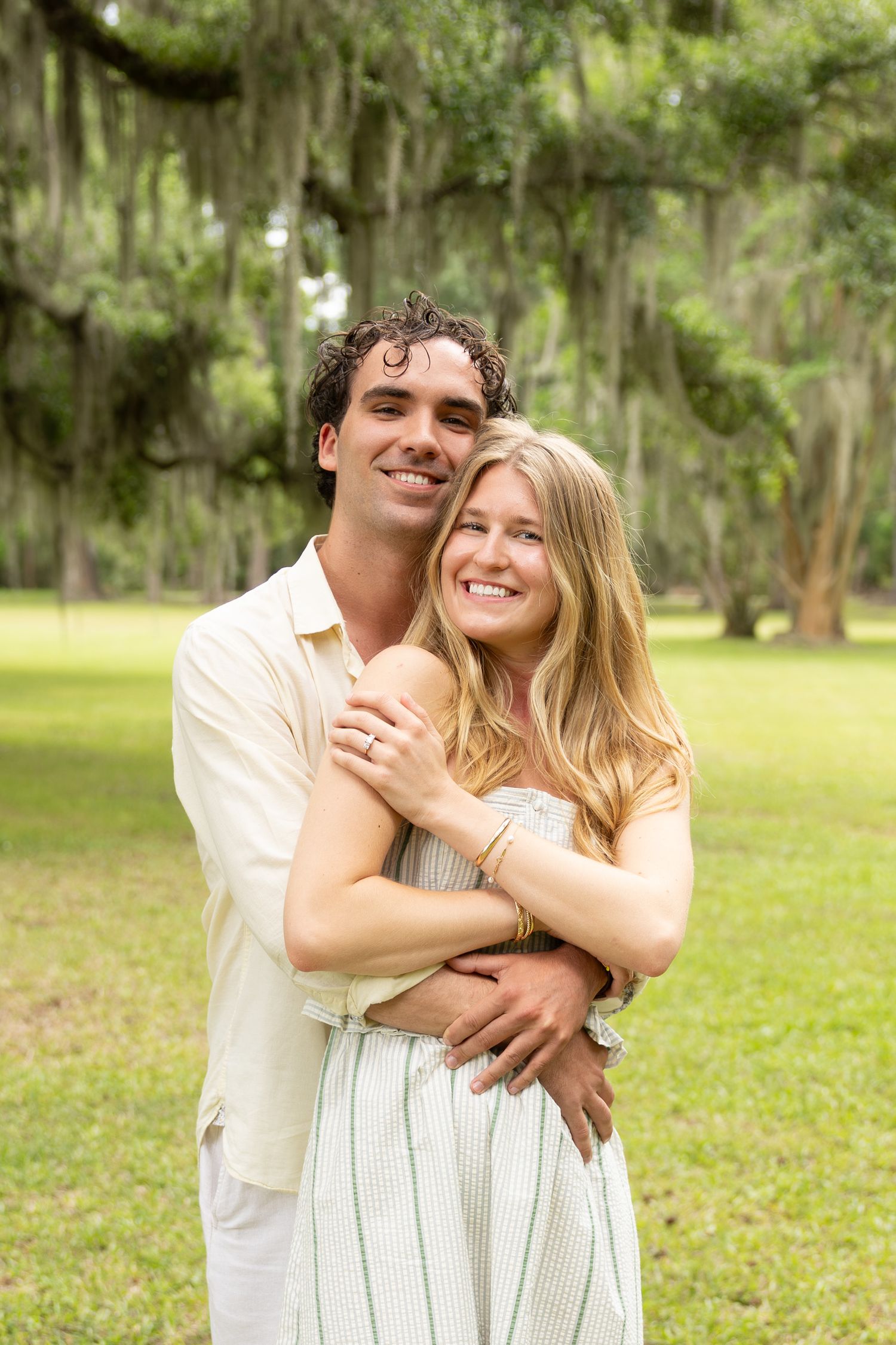 Happy couple embracing outdoors under Spanish moss-draped trees on a green lawn.