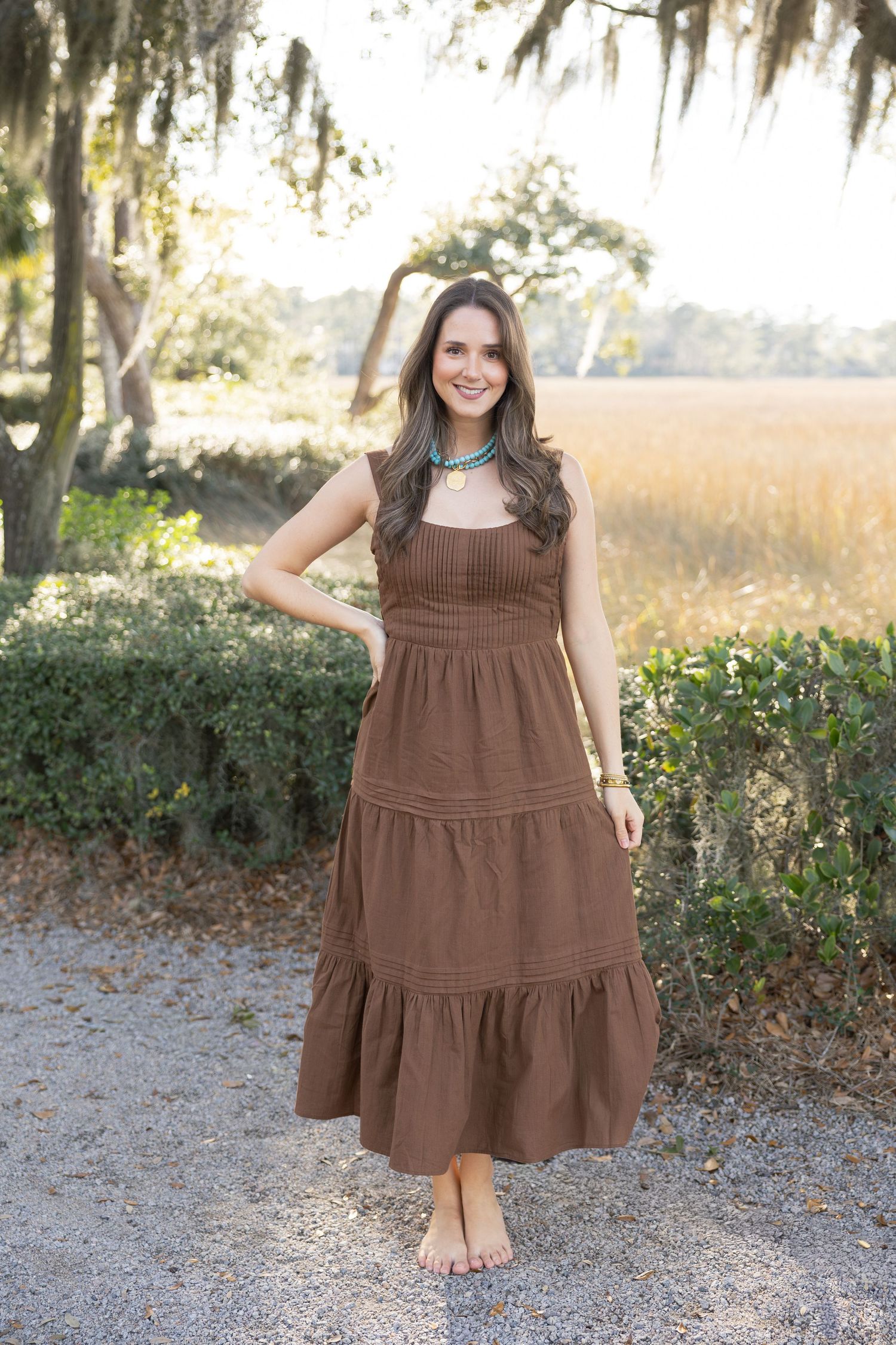 A brown tiered cotton dress with ruffles shown in multiple views against an outdoor garden background.