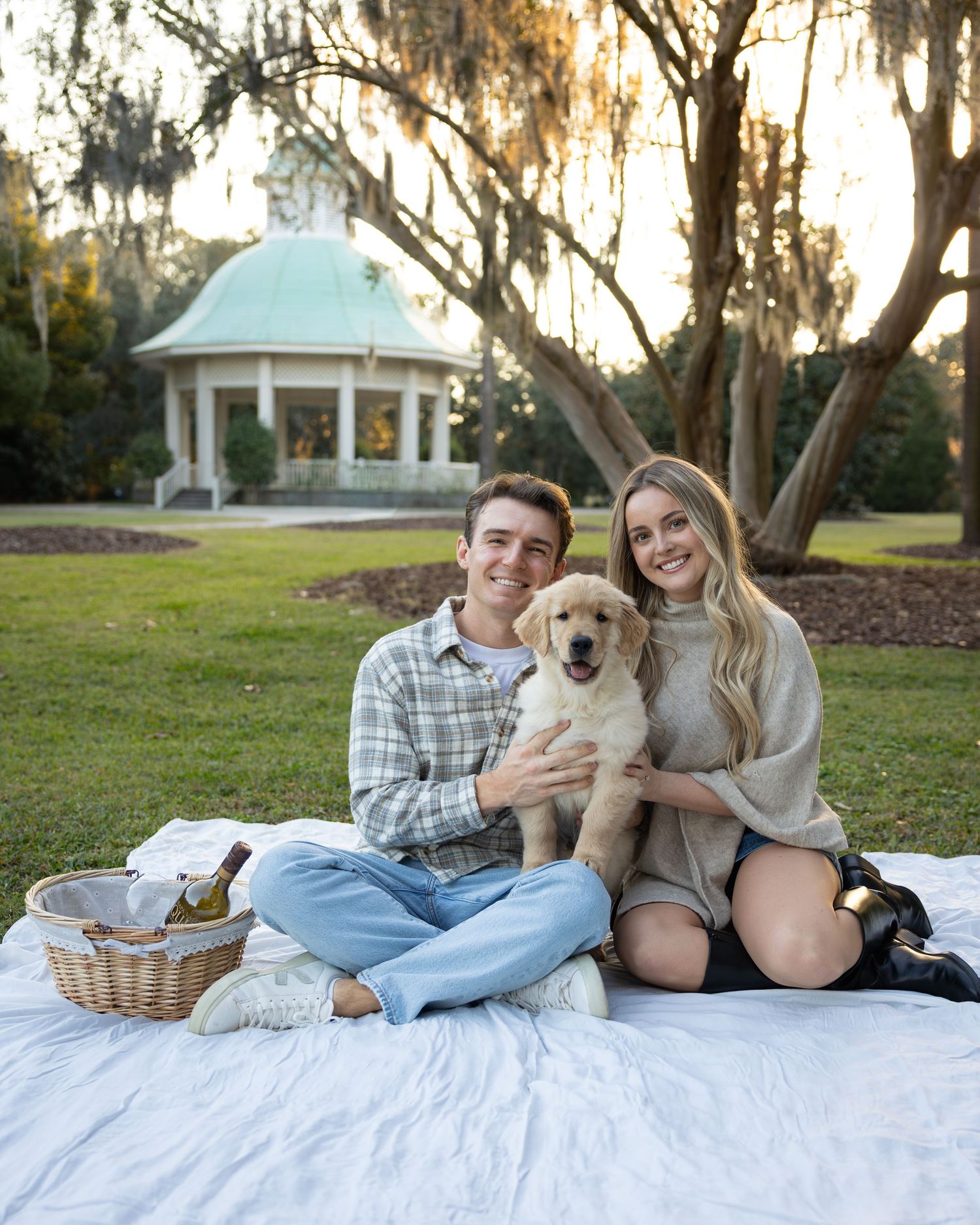 A couple relaxes on a white blanket with their dog during an outdoor photoshoot.