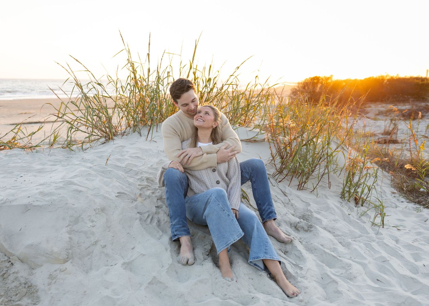 Couple relaxing on white sand dunes during sunset photoshoot.