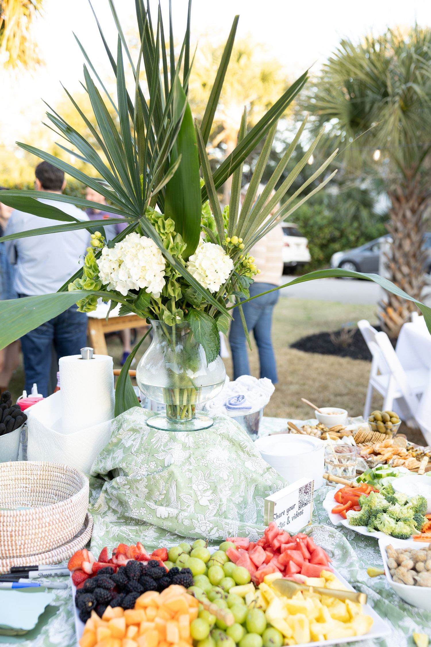 Elegant wedding reception buffet table with fresh fruits, tropical decor and white floral arrangements.