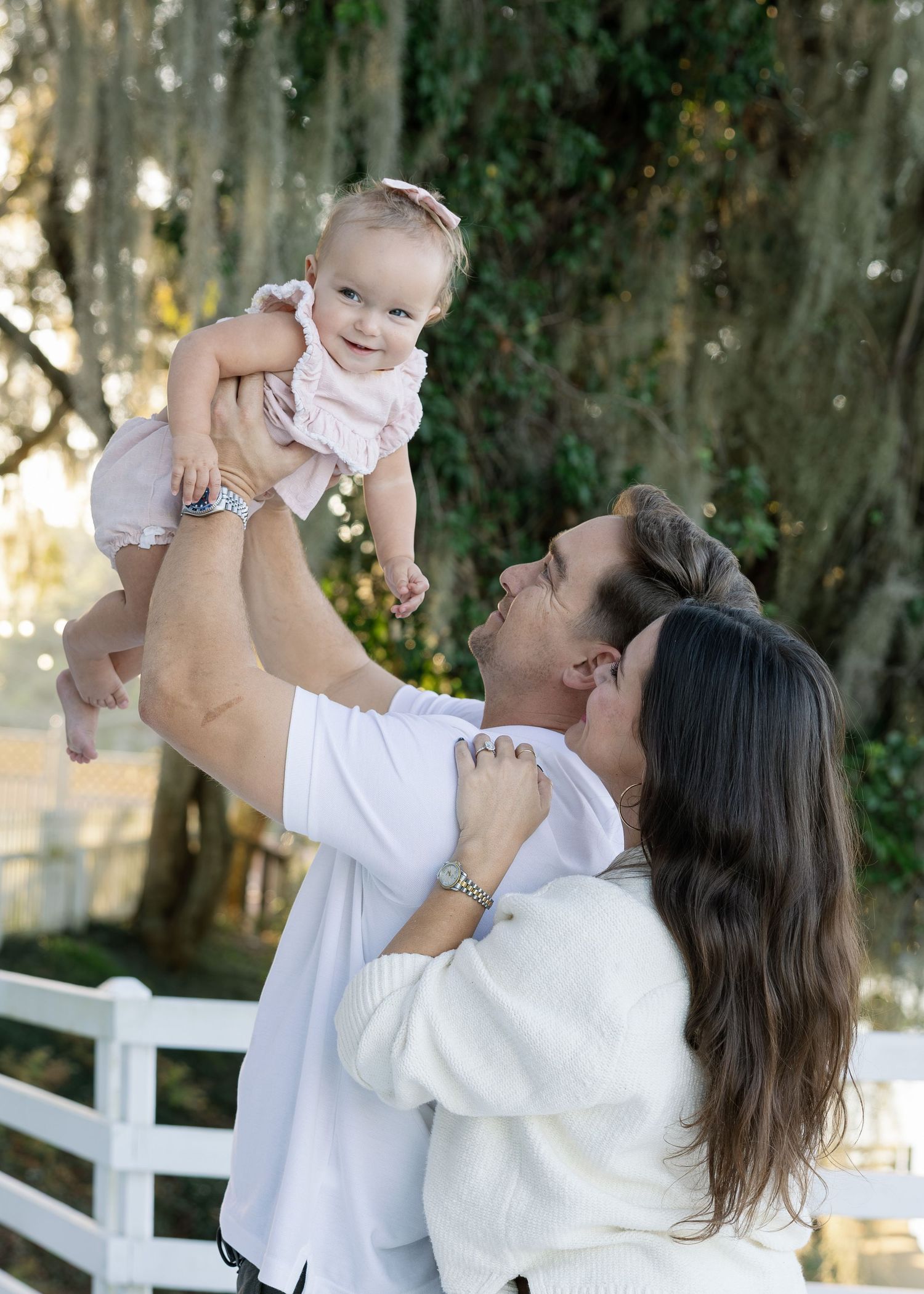 A tender moment captured in a series of photos showing a parent lifting and playing with a baby in white outdoors.