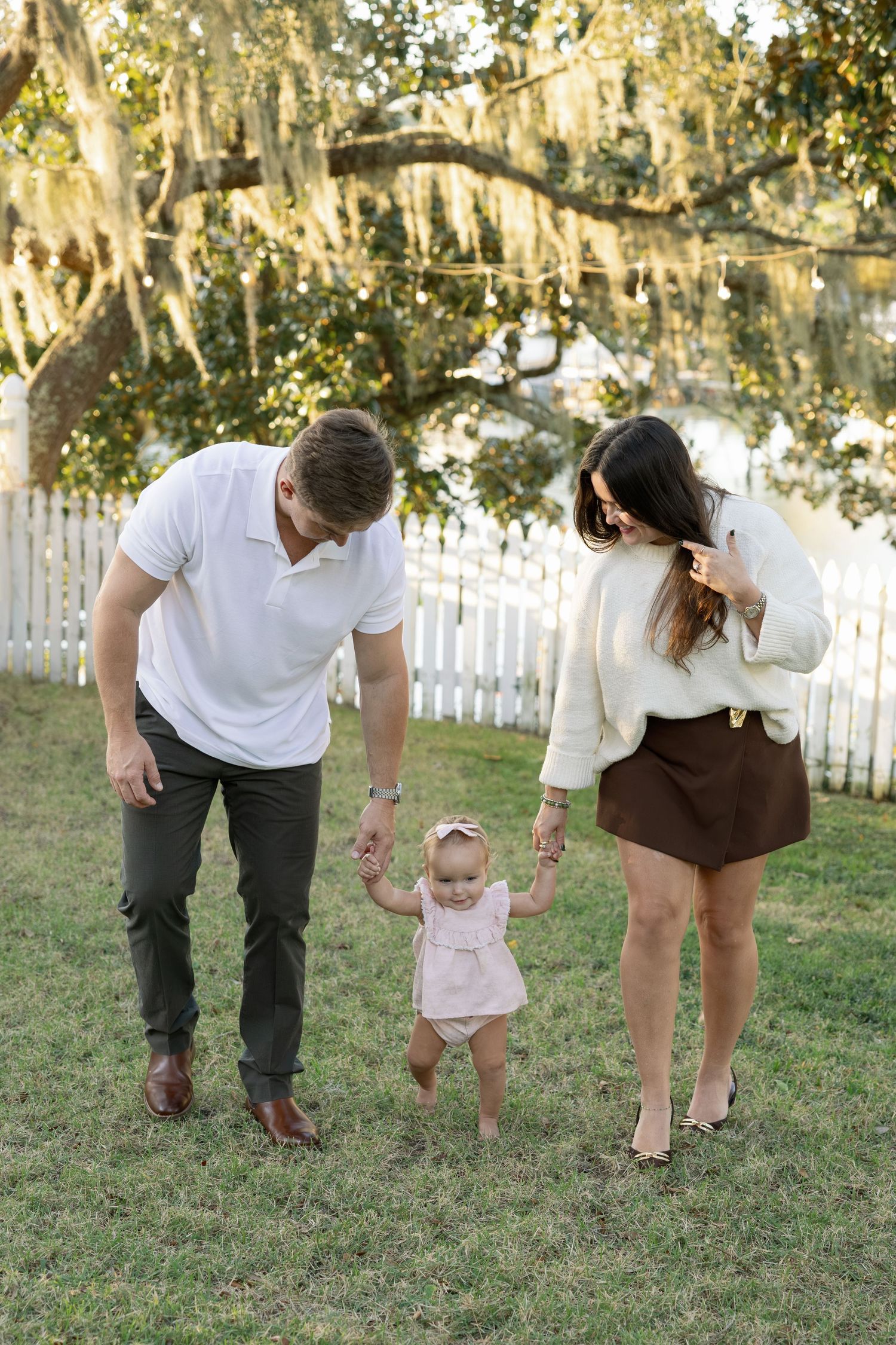 A sequence of photos showing adults helping a baby learn to walk on grass with a white picket fence in background.
