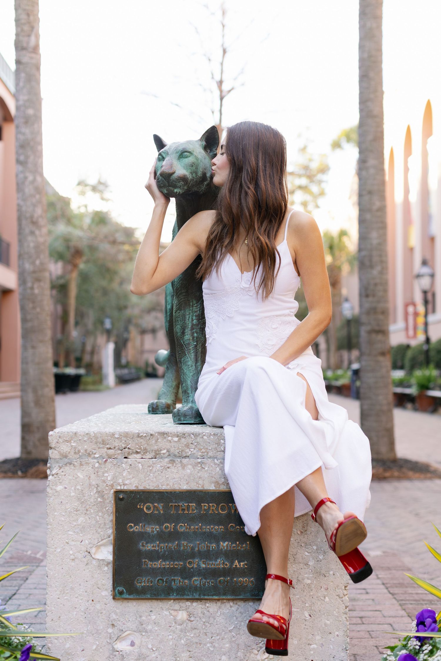 A person in a white dress sits on a stone bench near palm trees wearing red shoes, shown from multiple angles.