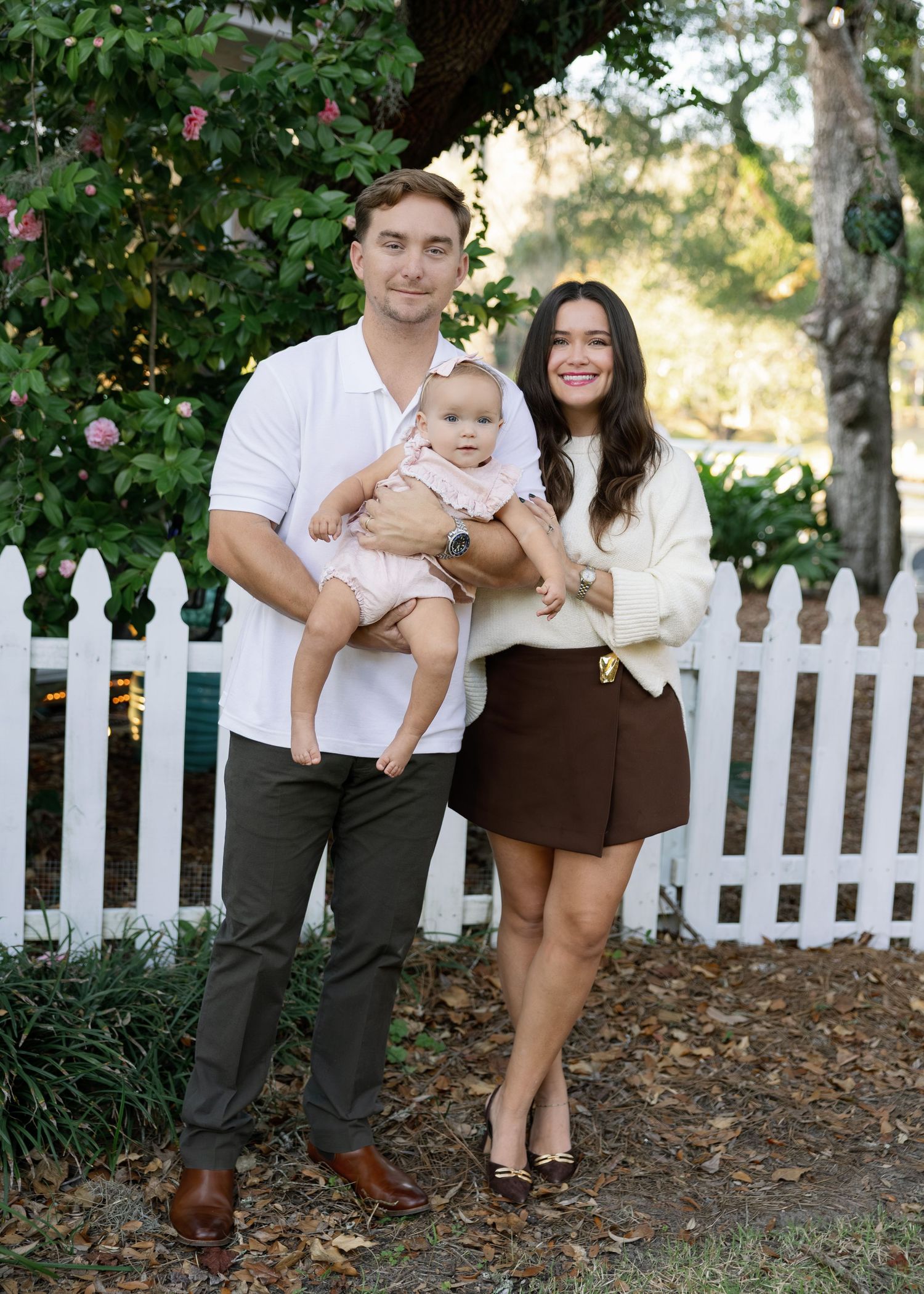A family poses for a series of casual outdoor photos in front of a white picket fence and flowering garden.