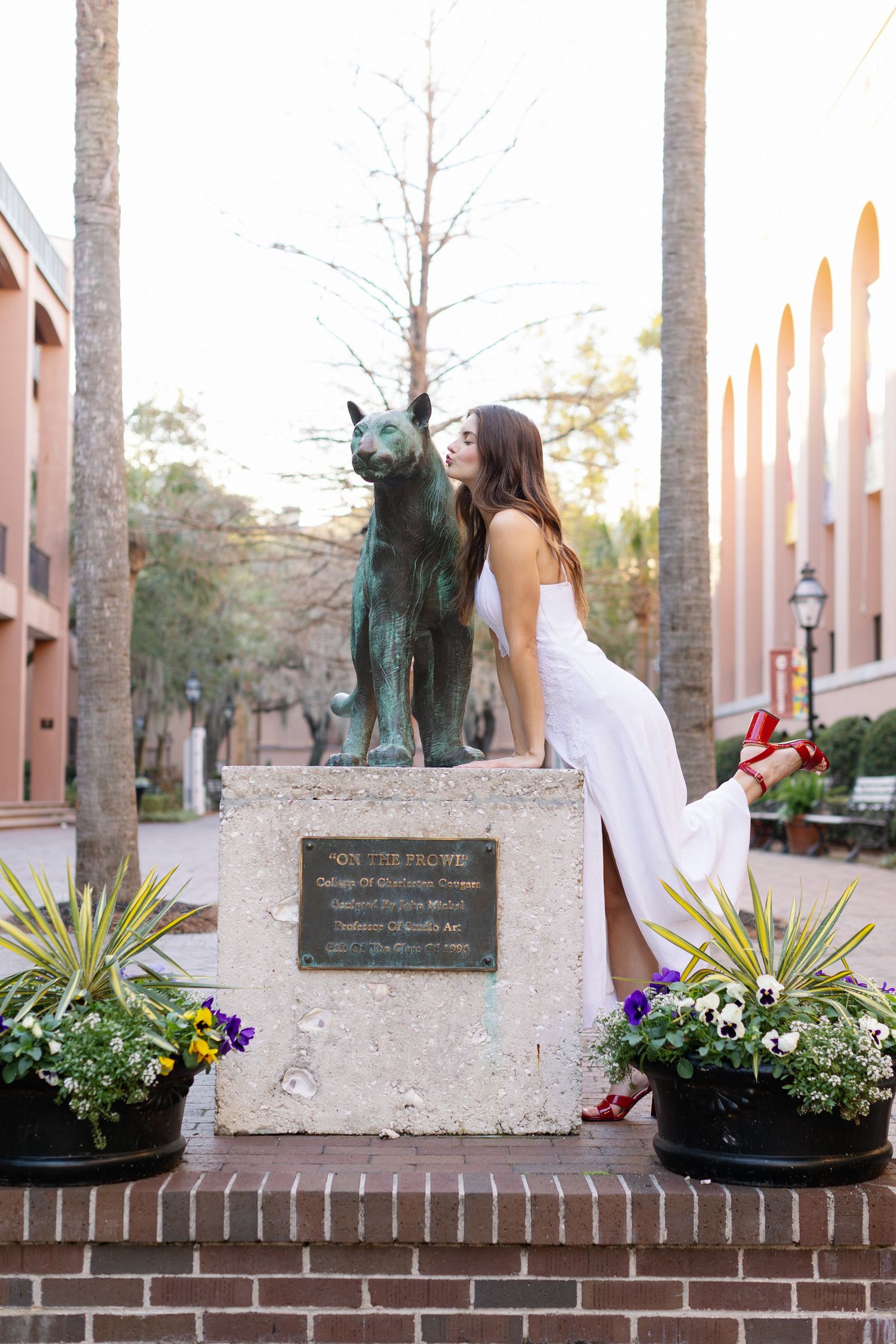 A white dress contrasts against brick planters filled with colorful flowers in an outdoor setting.