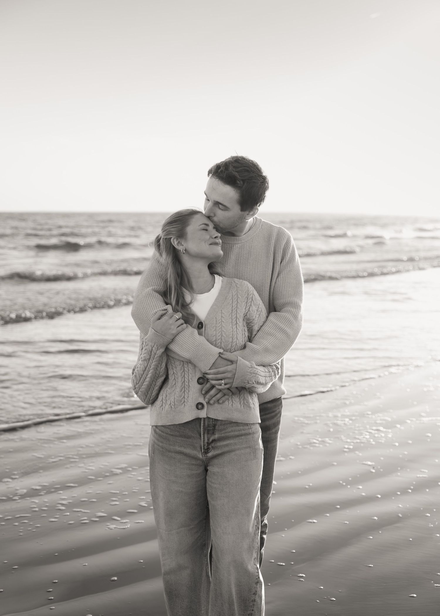 Romantic couple embracing on sandy beach at sunset in casual attire.