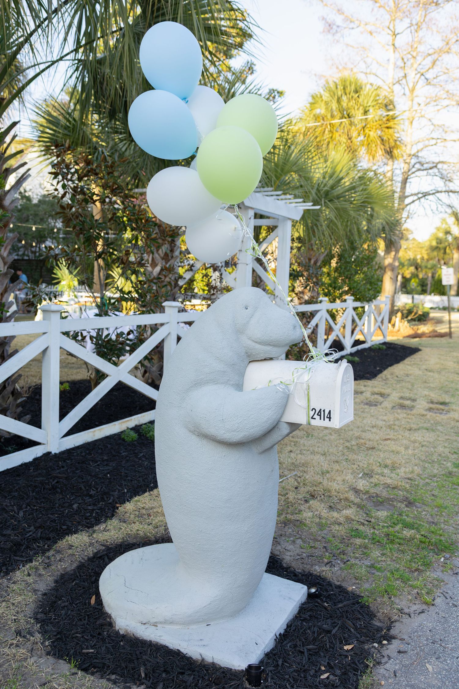 A series of four photos showing a concrete snowman statue decorated with colorful balloons against a white fence and palm trees.