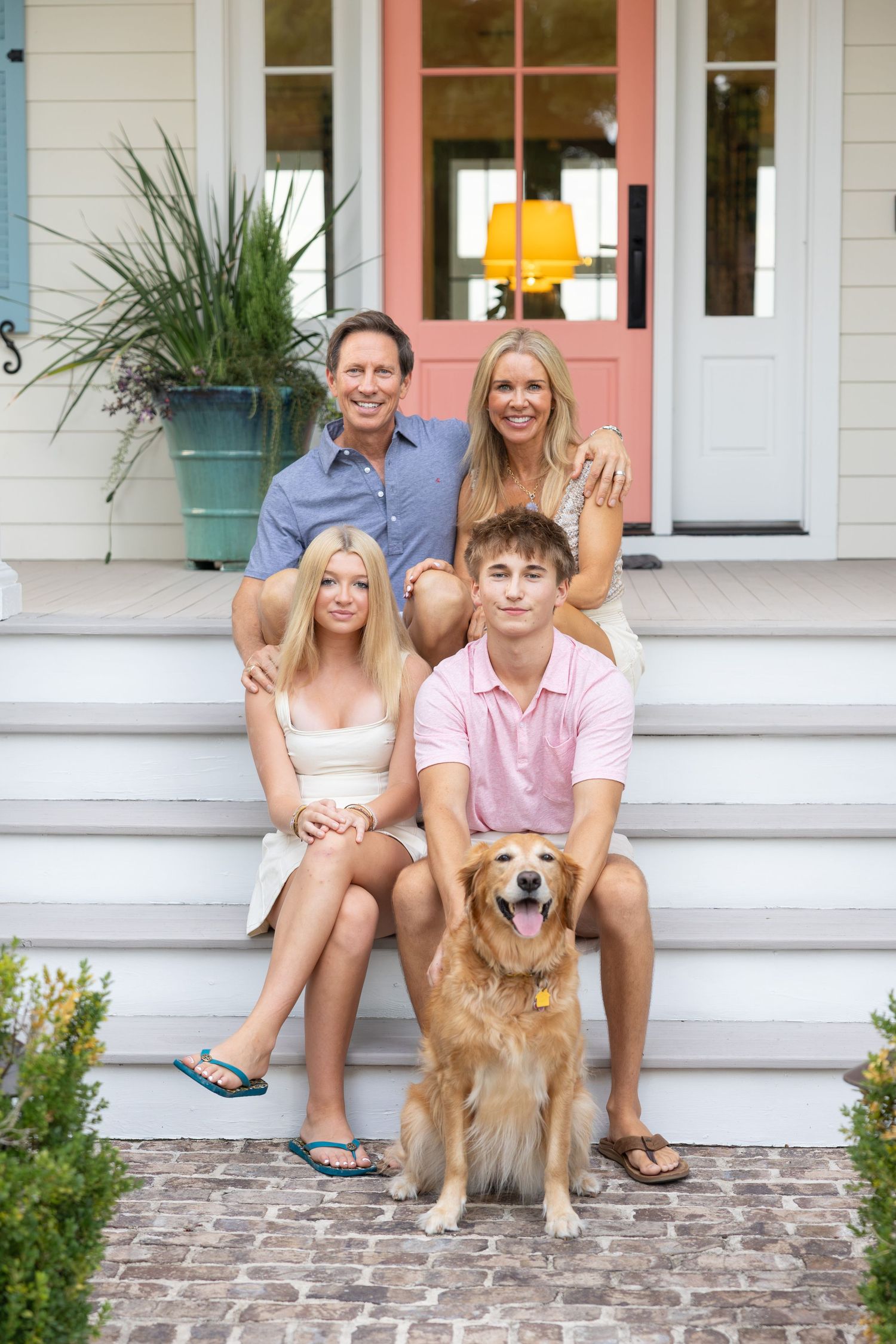 Happy family of four with golden retriever posing on front porch steps of charming home.