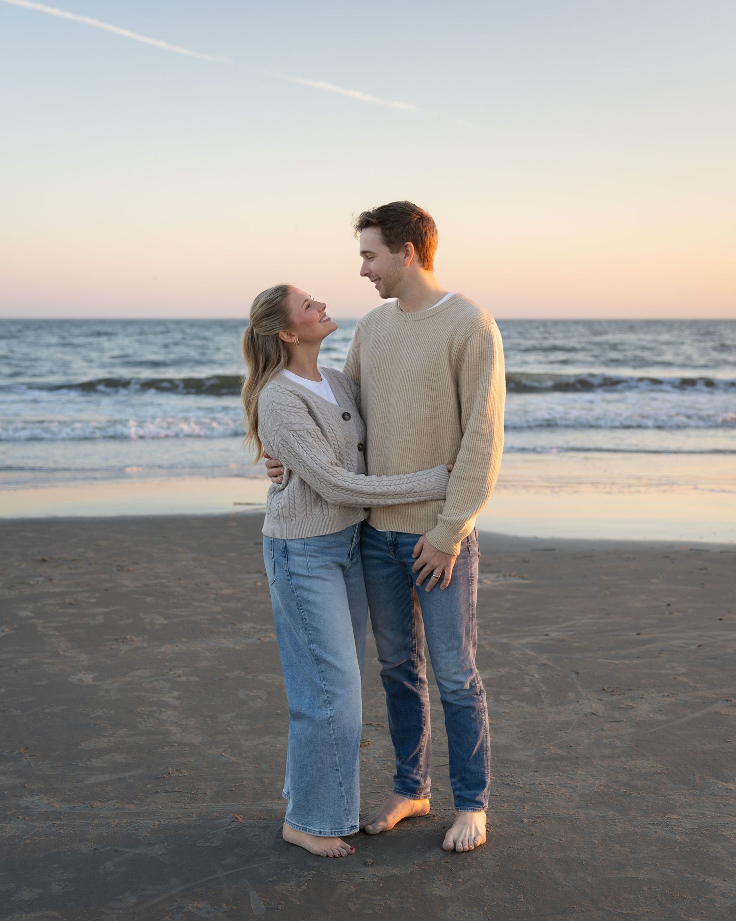 A couple embraces on a beach at sunset wearing casual denim and neutral colors.
