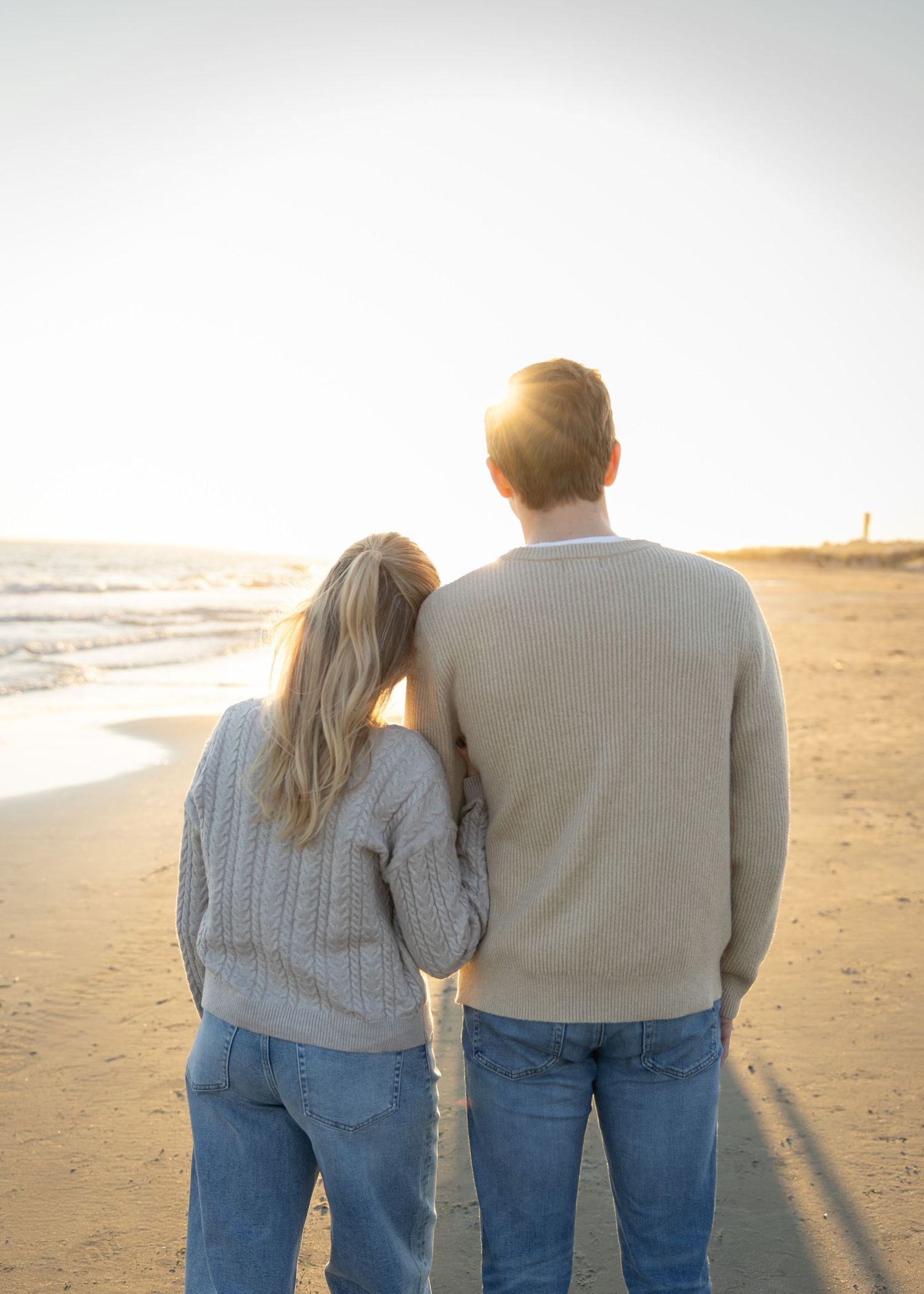 Couple walking together on beach at sunset wearing matching casual outfits.