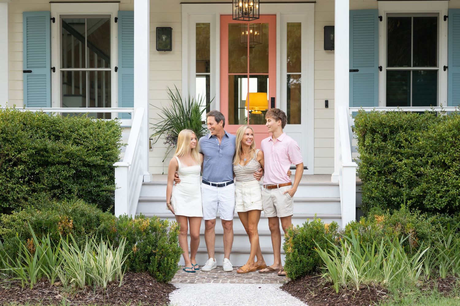 Four smiling friends pose together on the front porch steps of a charming white Southern-style home.