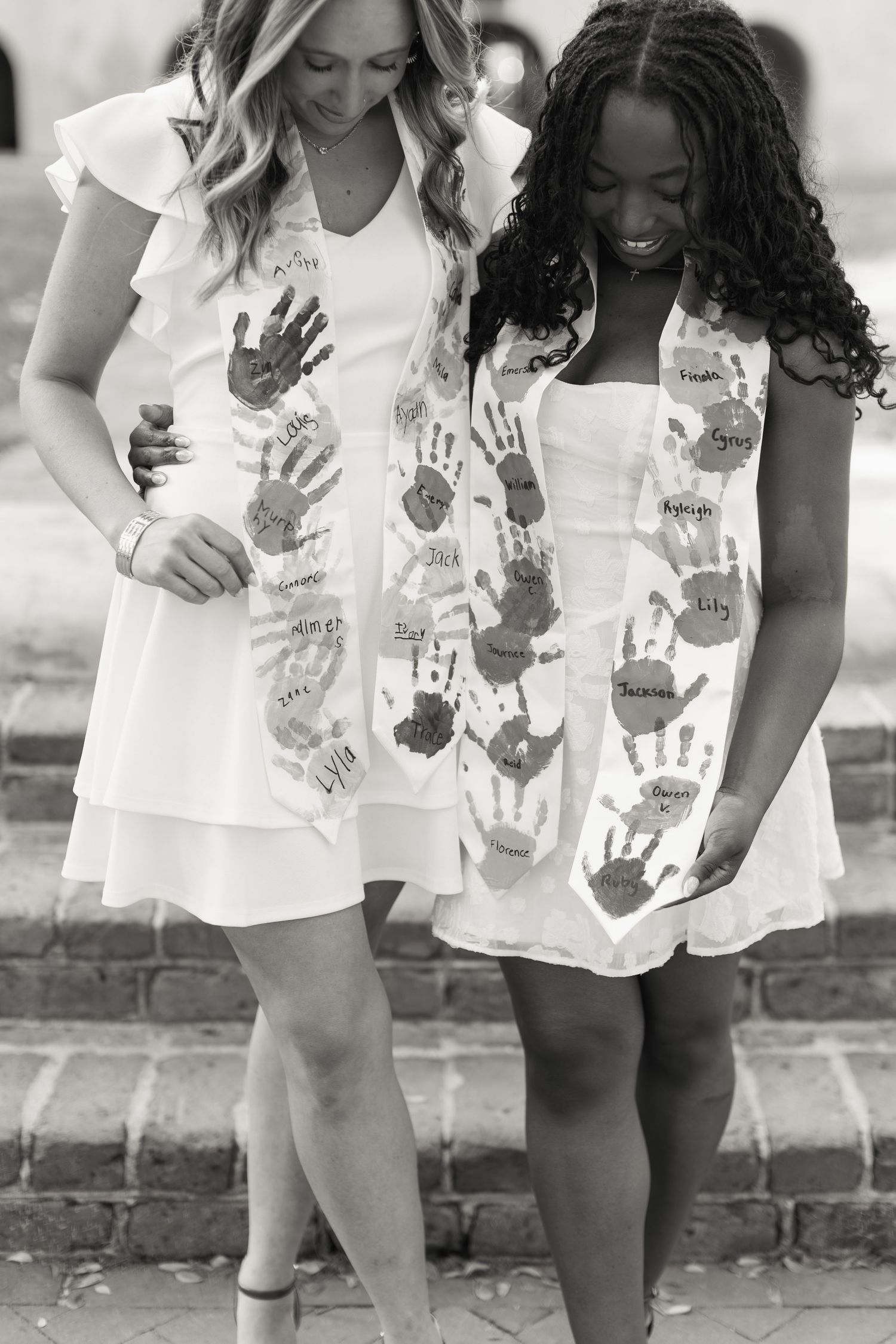 Two women in white dresses with colorful handprints and signatures stand on steps in black and white photo.