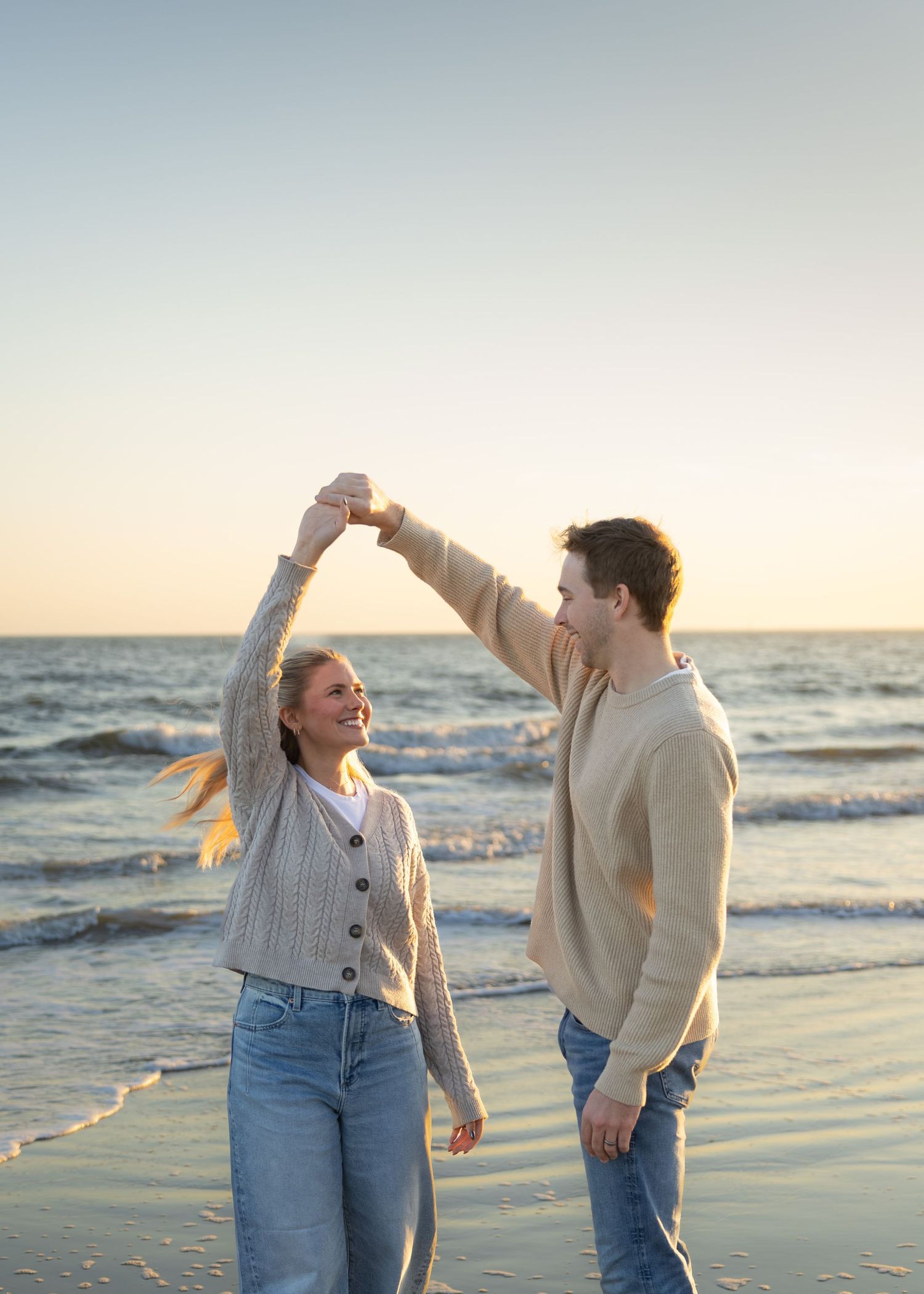Couple dancing playfully together on beach during sunset.